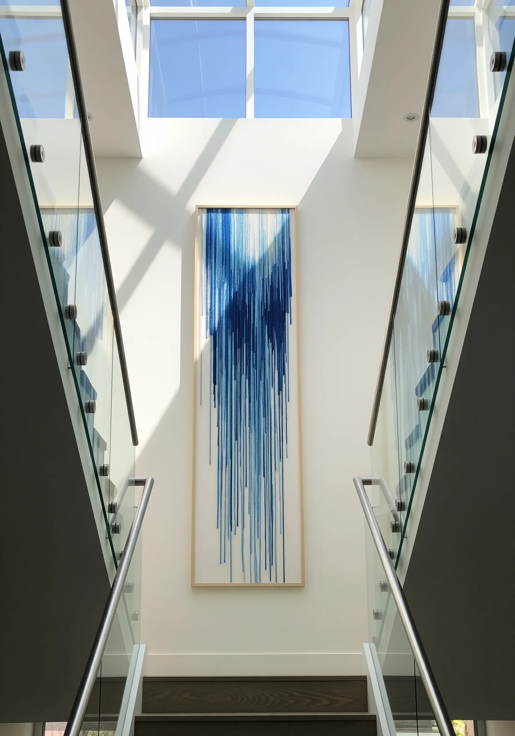 A tall, framed piece of fiber art showing blue threads cascading down like a waterfall.