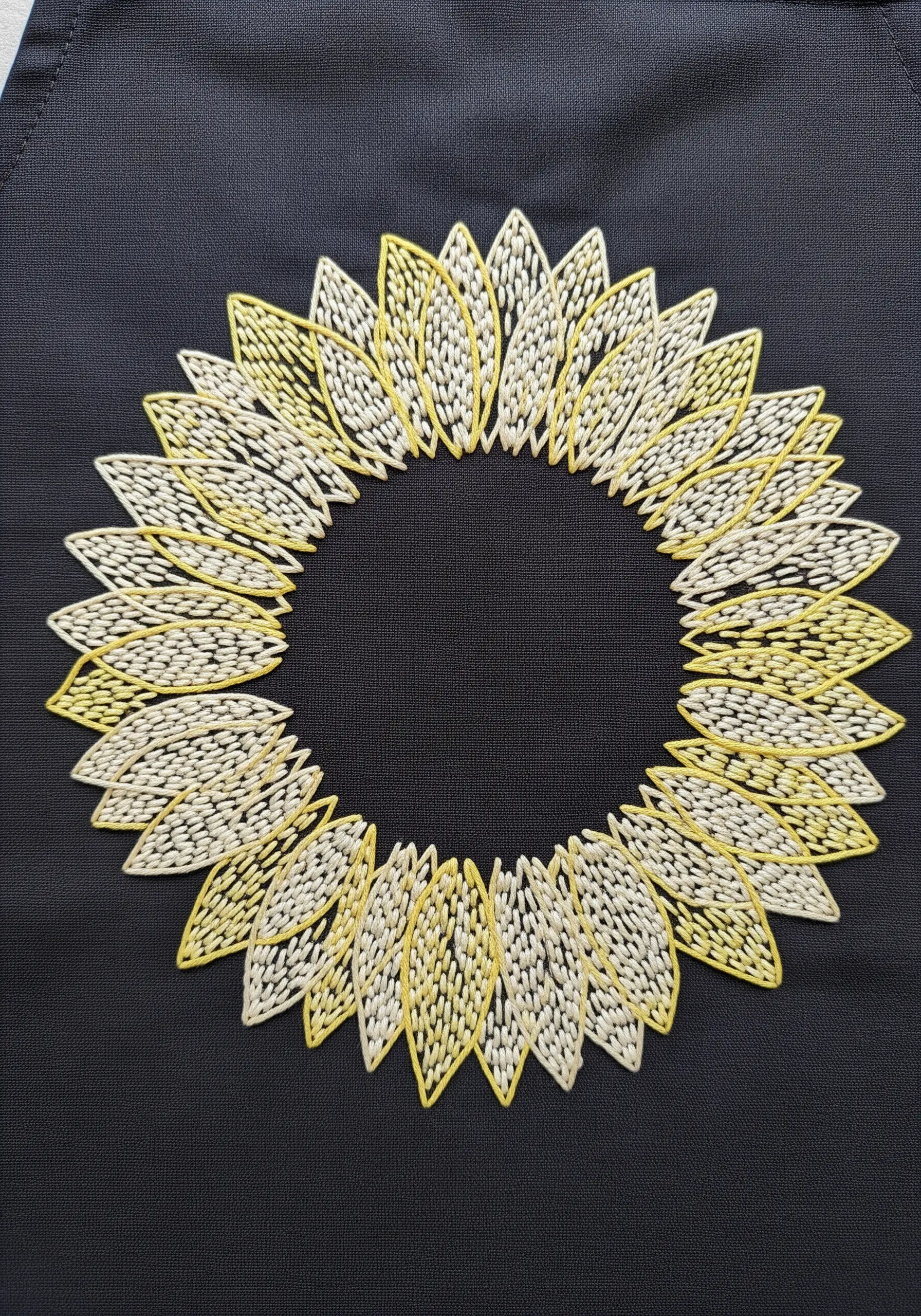 A sunflower motif embroidered with open-weave fill stitches, creating a light and airy petal effect
