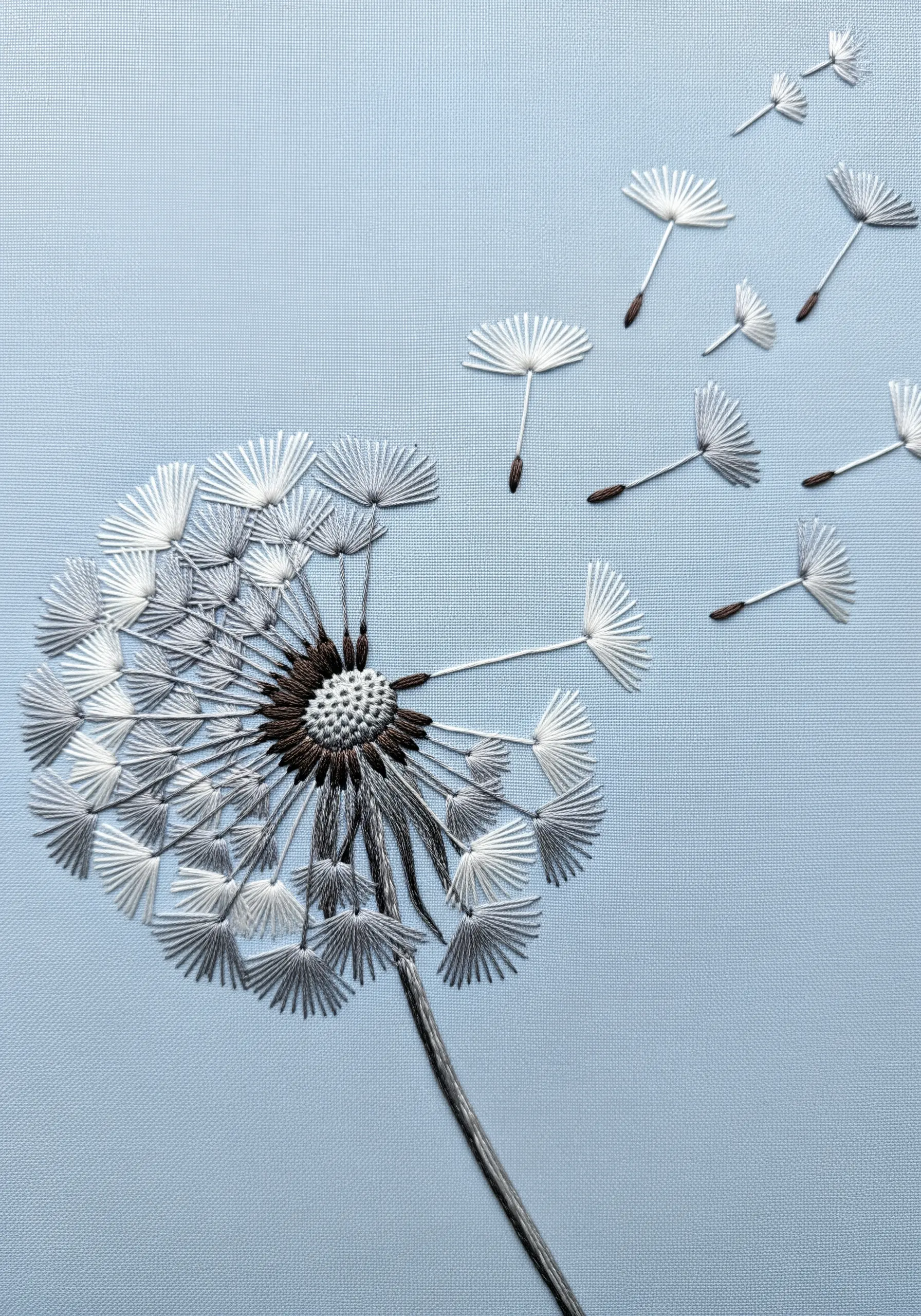 A dandelion with seeds blowing away, stitched with delicate white and grey threads.