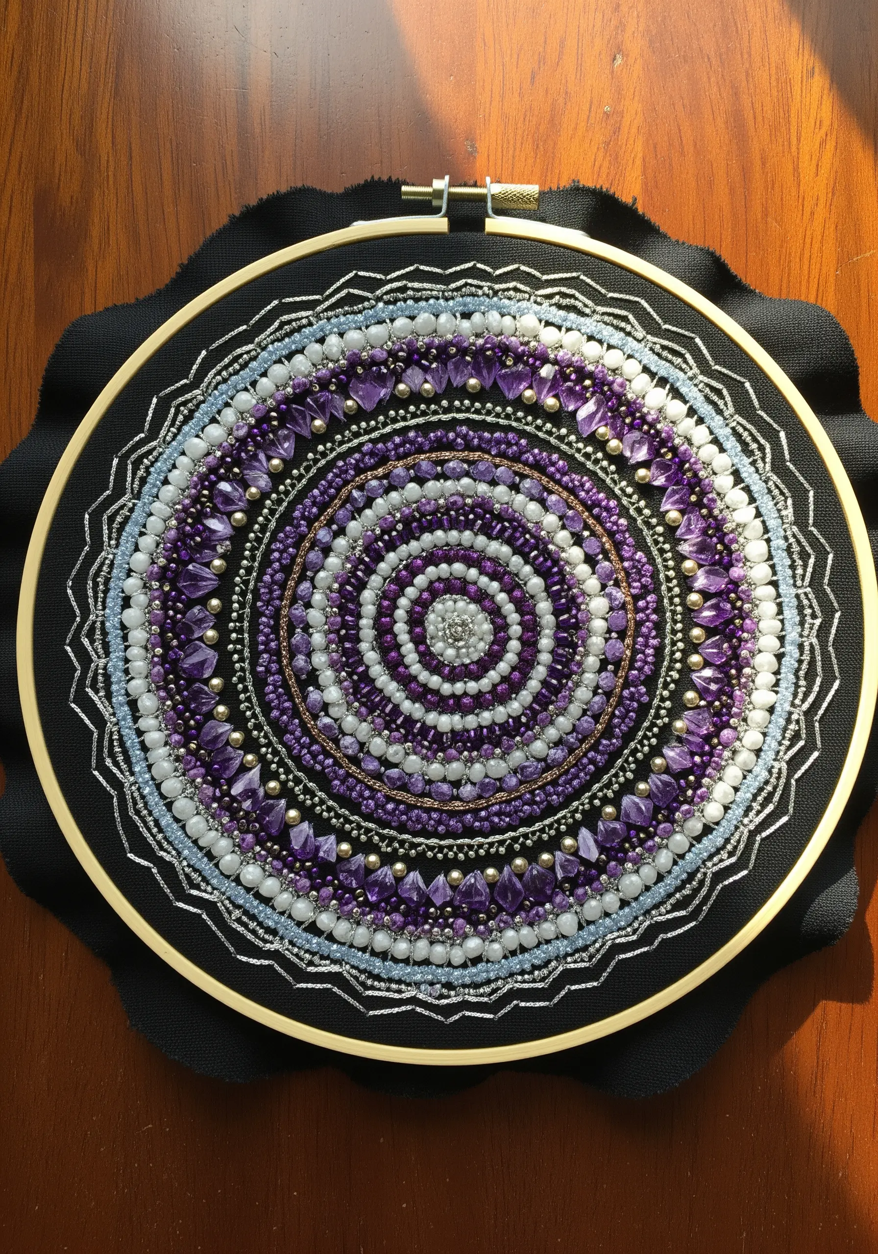 A detailed mandala made with purple, silver, and white beads on black fabric.