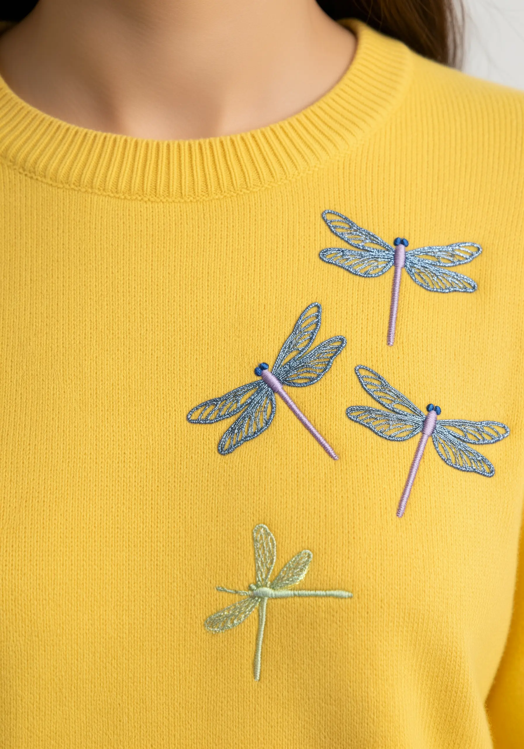 Three embroidered dragonflies with sheer, open-stitched wings on a yellow sweater.