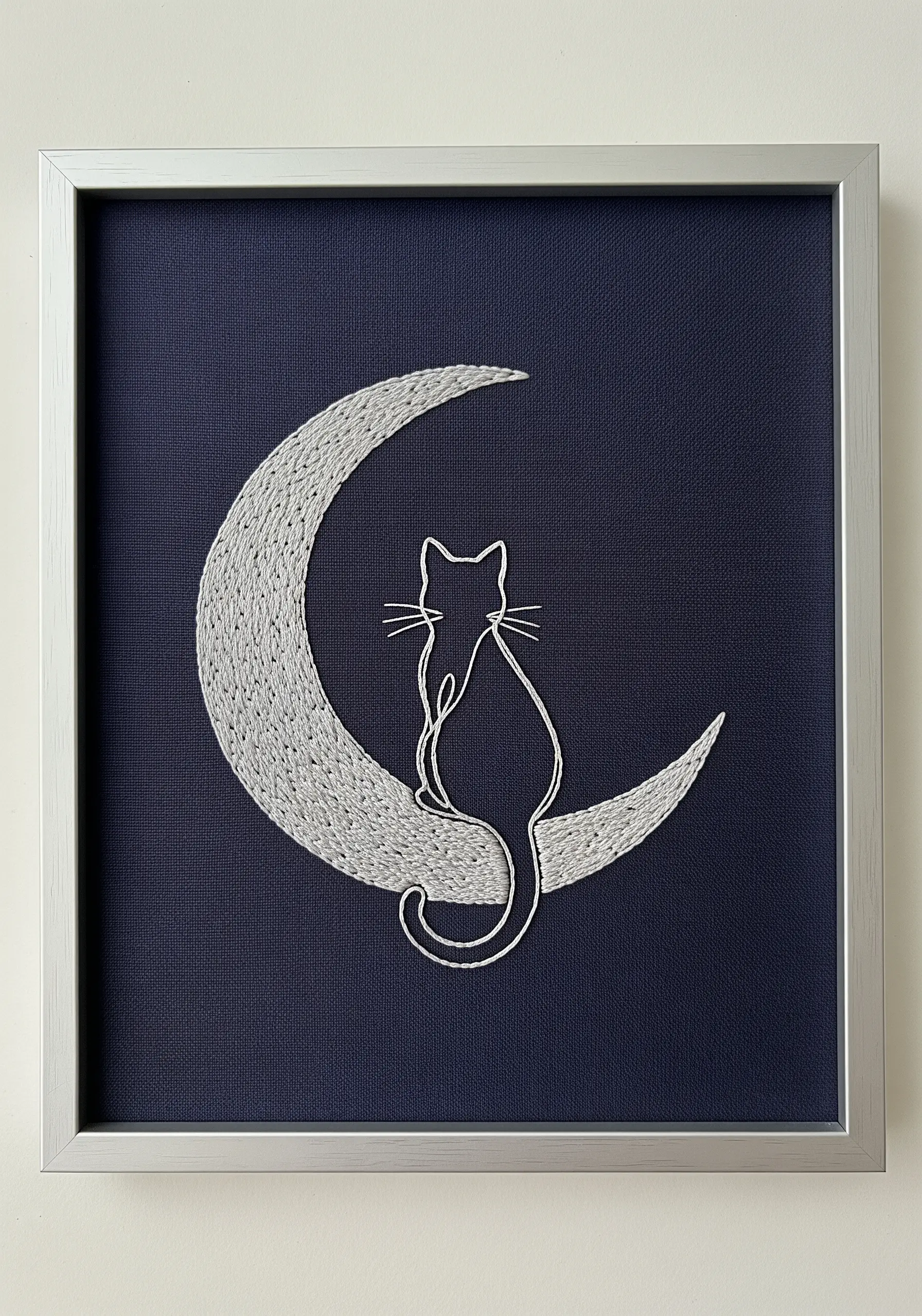 A line art cat sitting on a heavily stitched satin-fill moon against navy fabric.