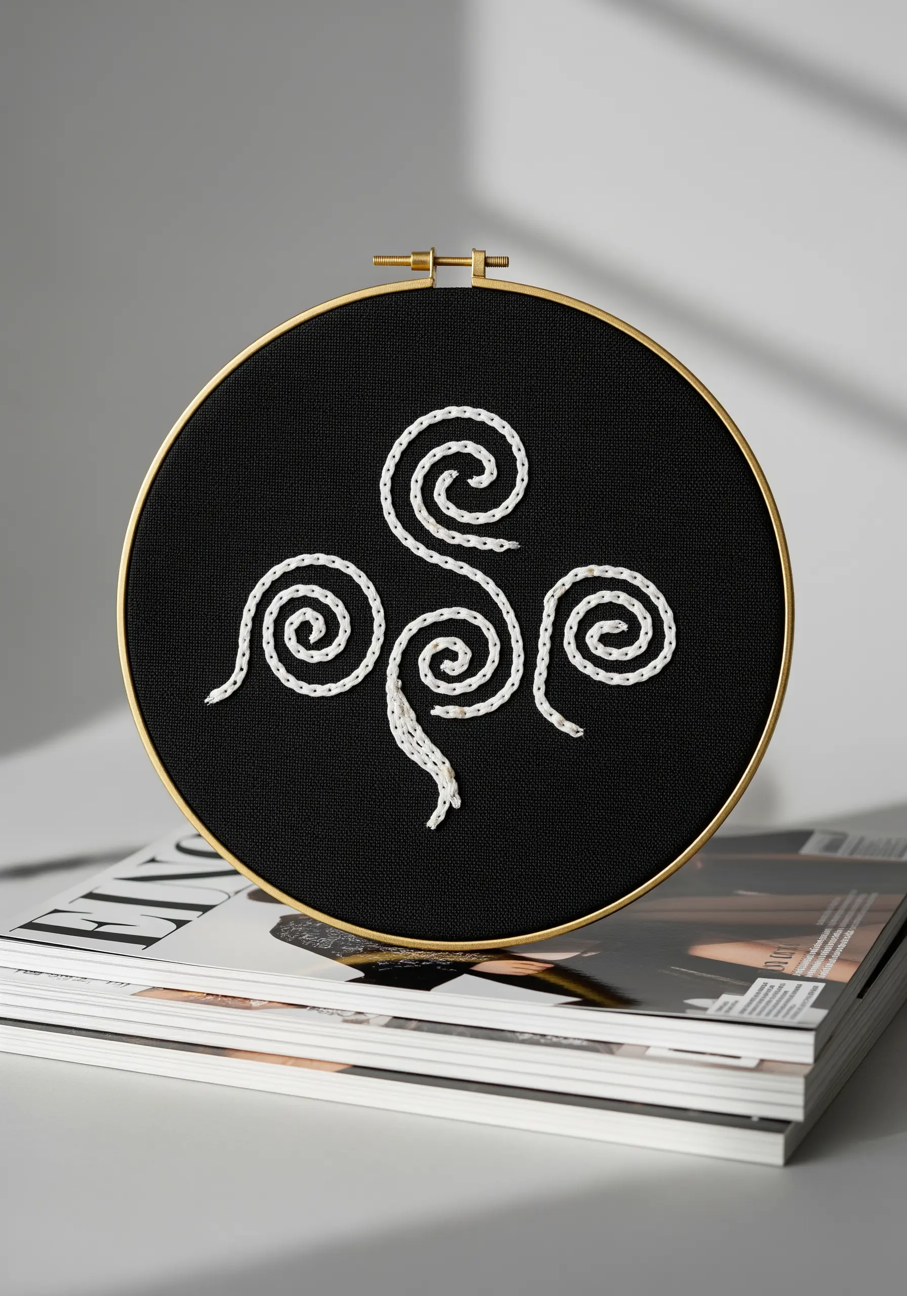 Abstract Celtic knot design with three spirals stitched in white on black fabric.
