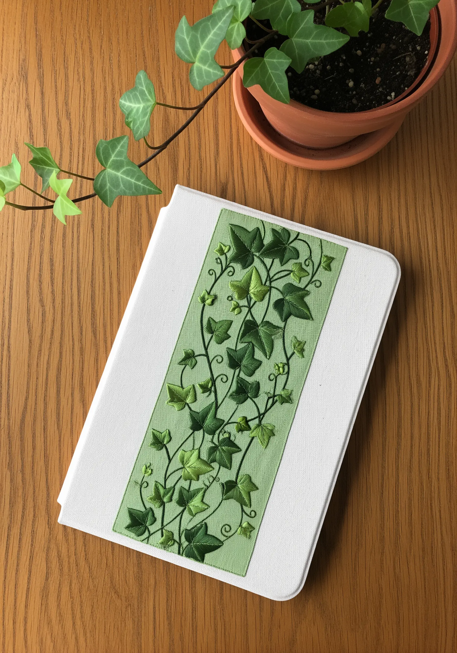 An embroidered panel of overlapping green ivy leaves on a white book cover.