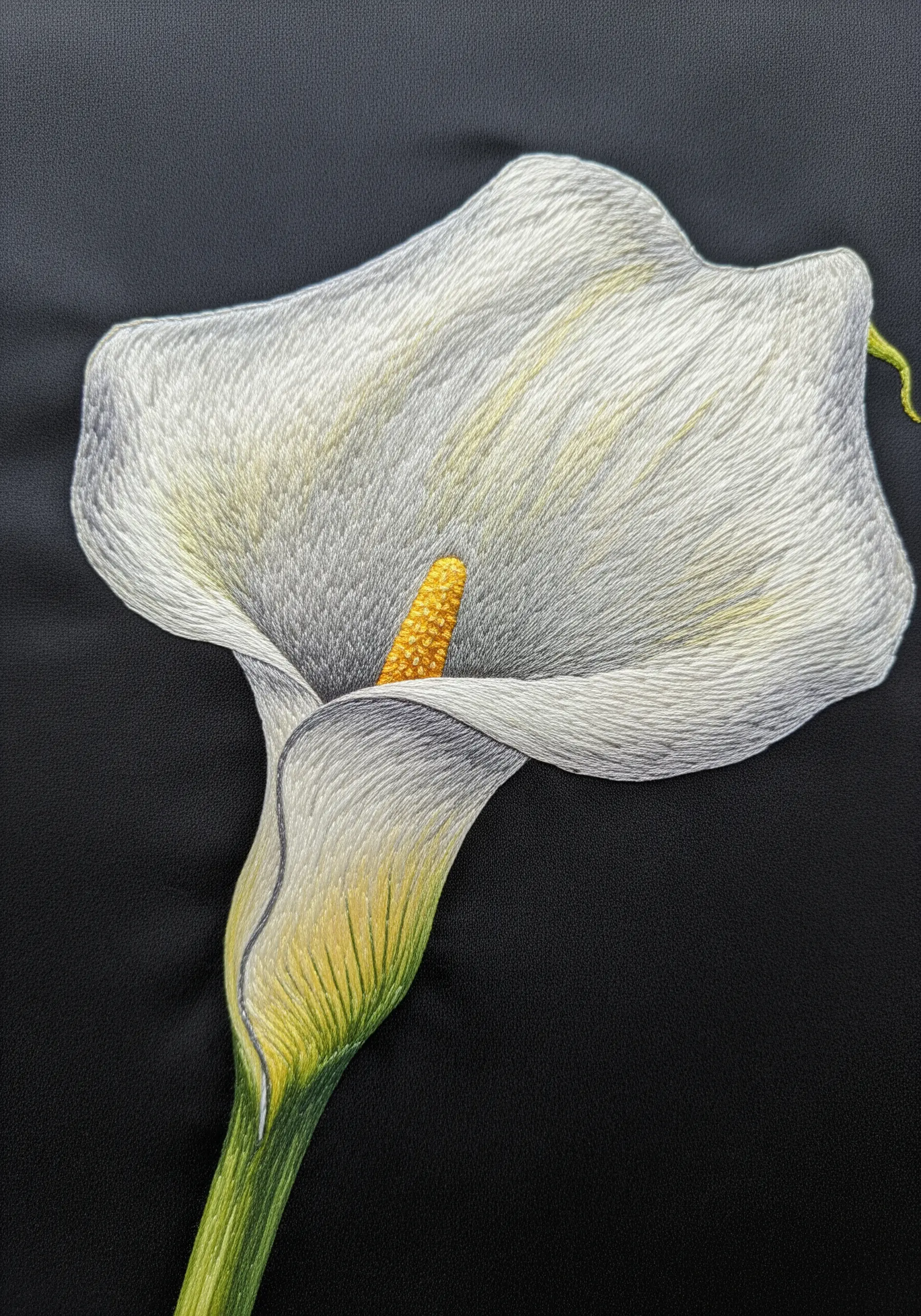 A white calla lily embroidery showing subtle shading with gray and yellow threads.