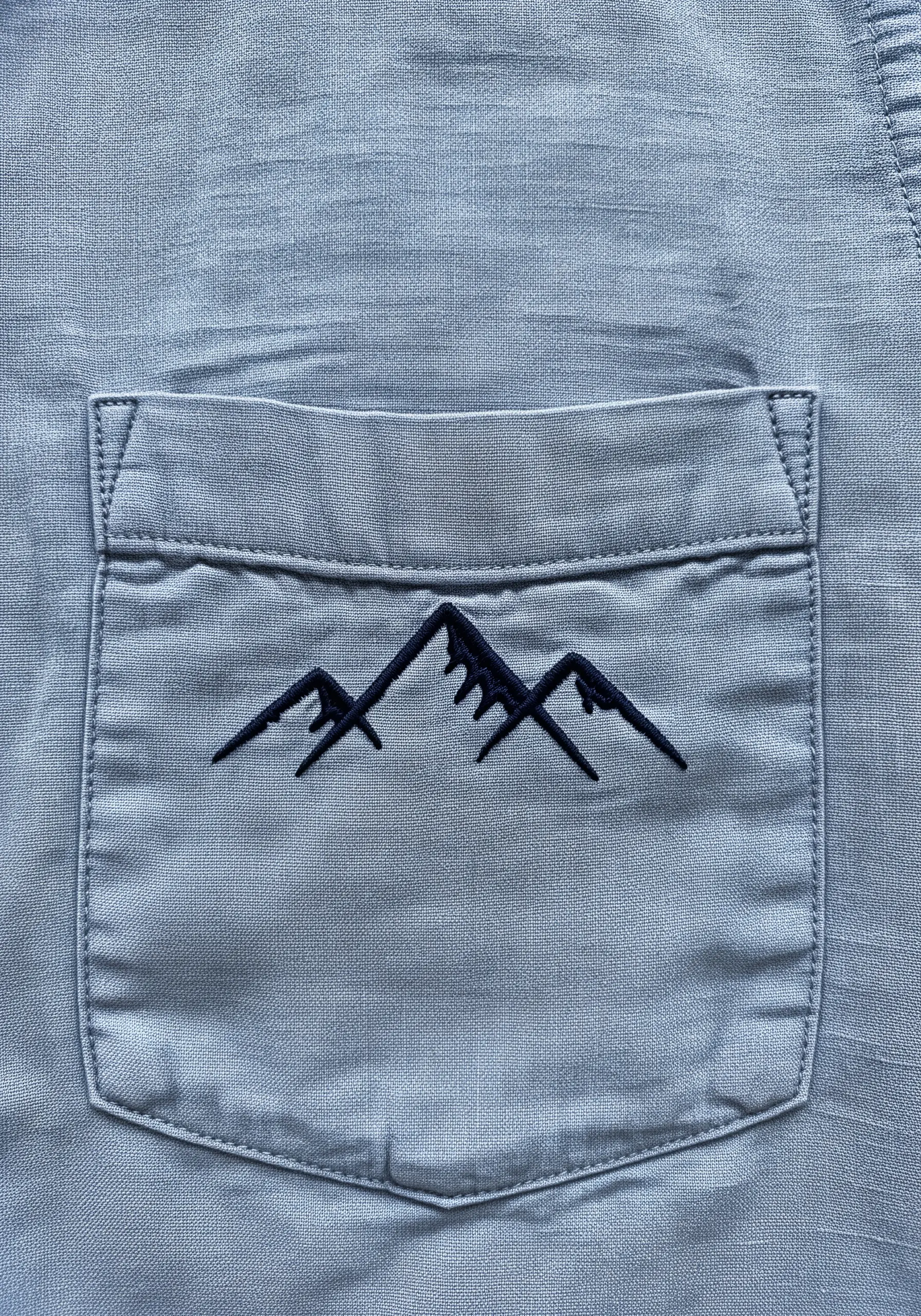 A simple black mountain range embroidered on a blue linen shirt pocket.
