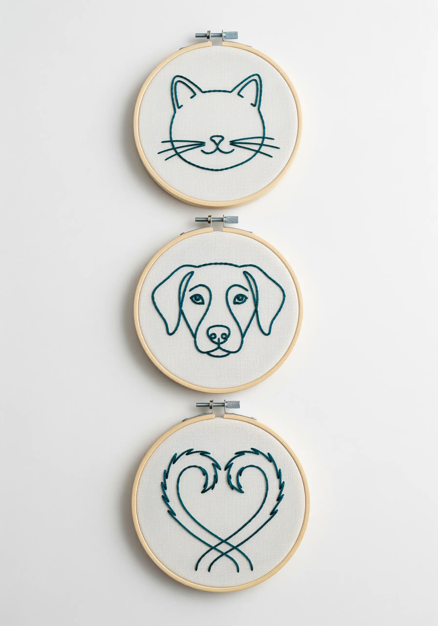 Three small embroidery hoops with a cat, a dog, and a heart in the same teal thread.