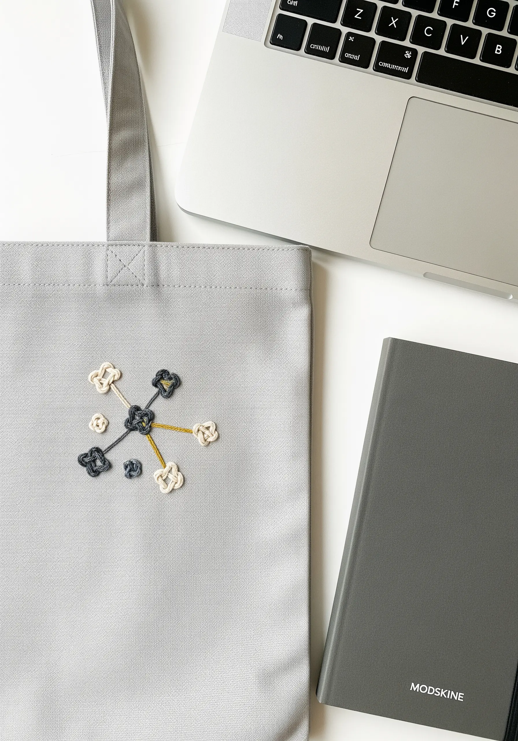 Abstract molecule-like design embroidered with grey, cream, and gold thread using textured knots.