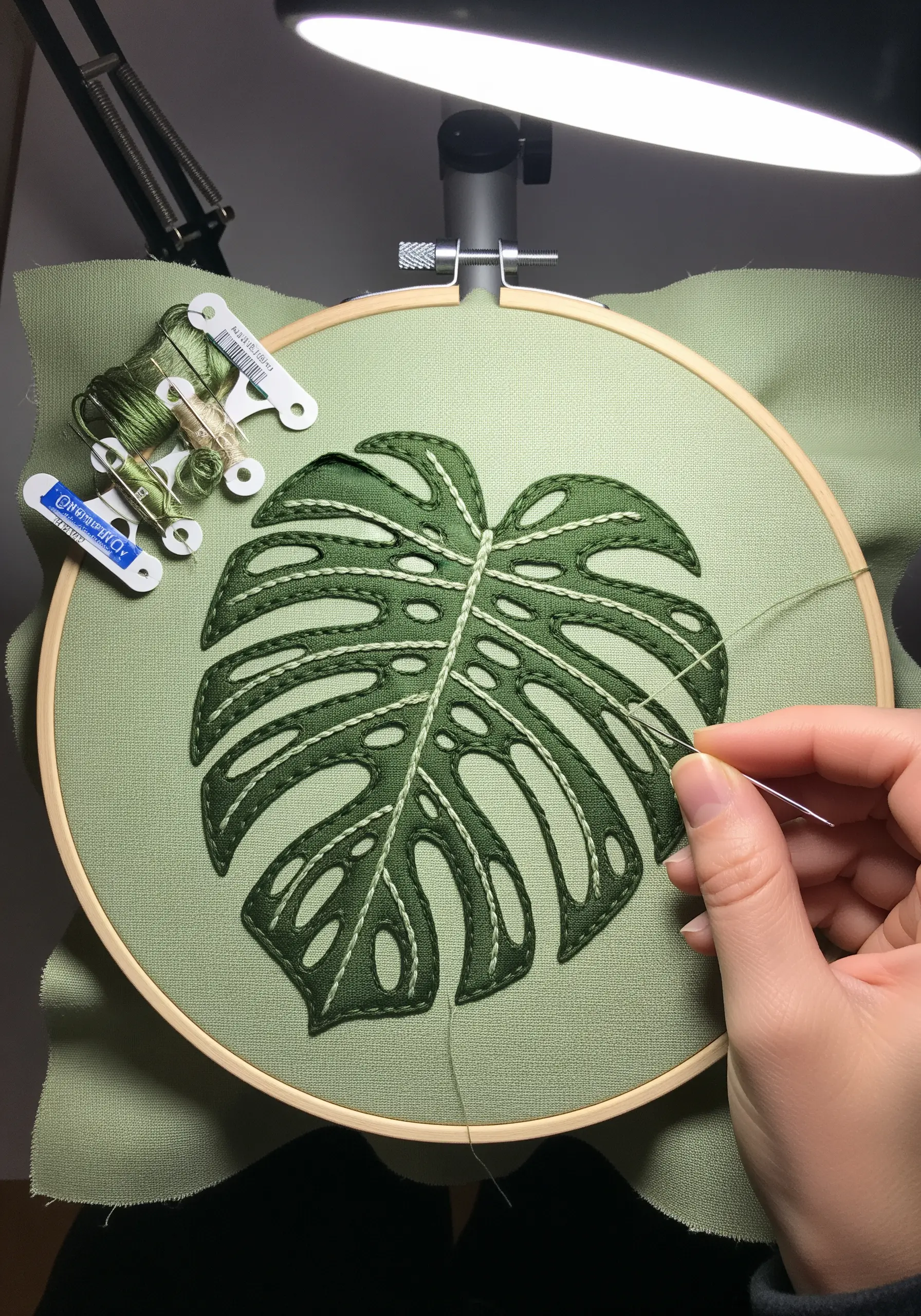 A green appliqué Monstera leaf outlined with off-white backstitching on light green fabric.