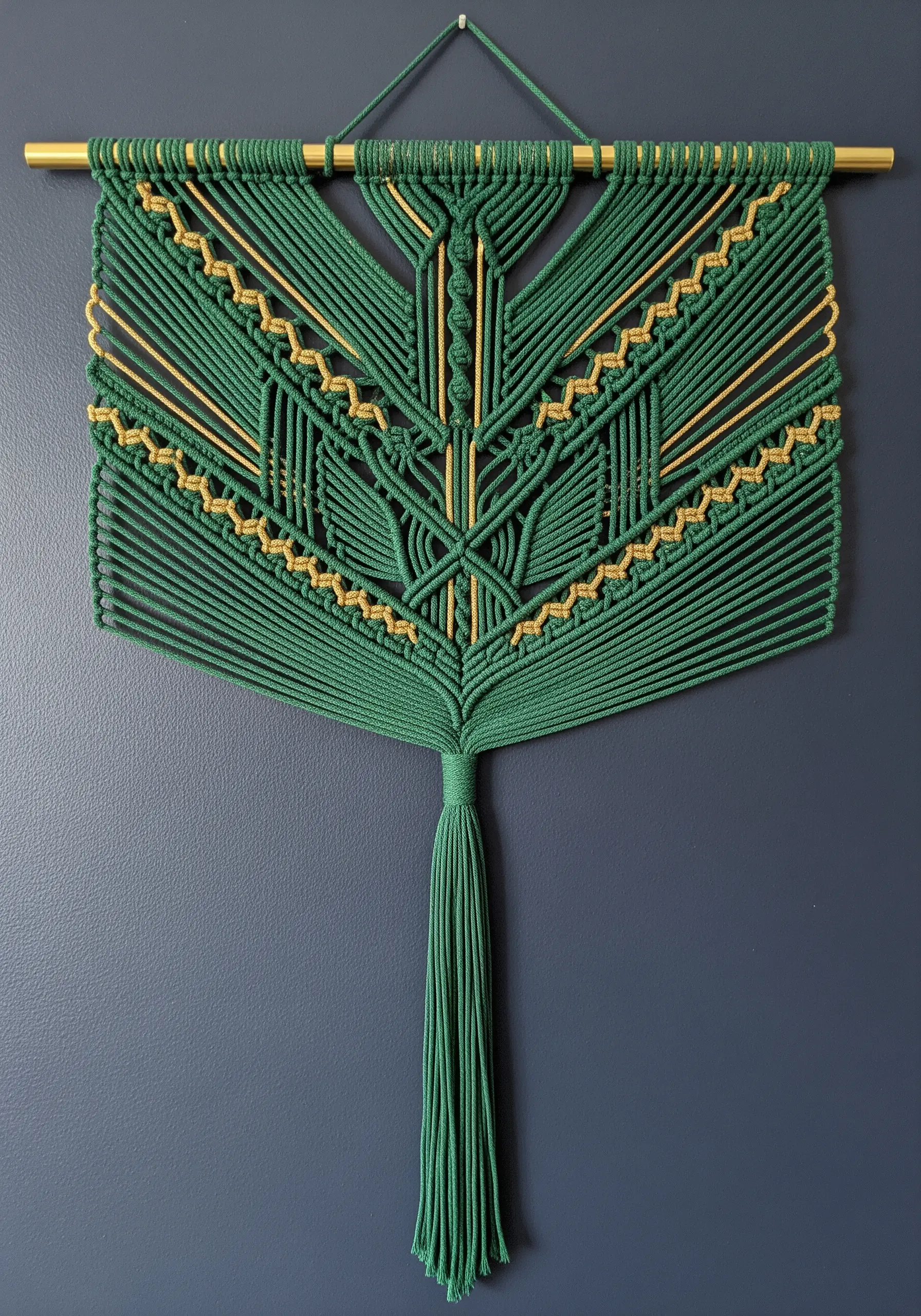 Intricate green and gold geometric macrame wall hanging with a large central tassel.