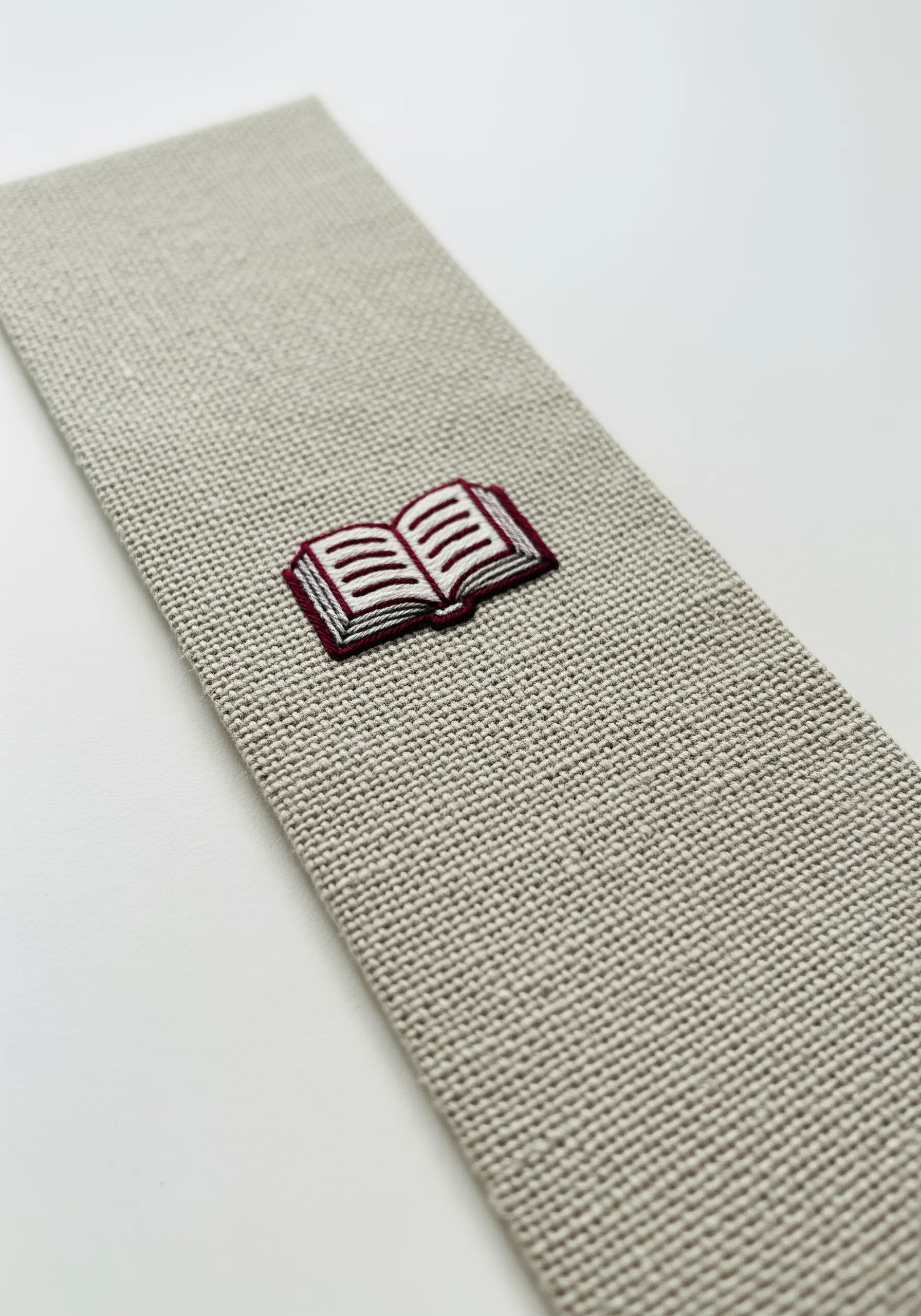 A tiny embroidered open book with red cover on a linen bookmark.