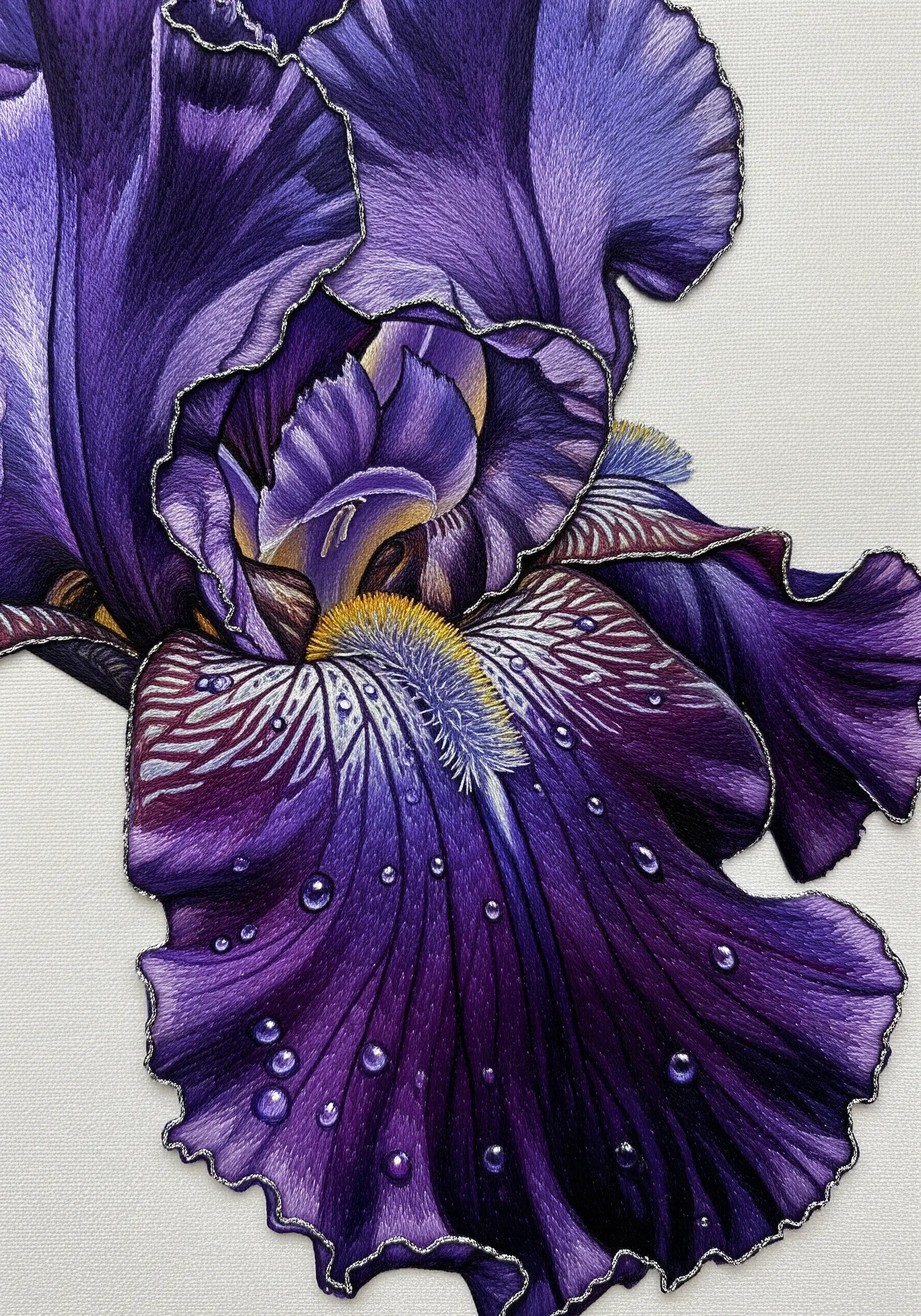 Close-up of a purple iris embroidery with metallic thread outlining the ruffled petals.