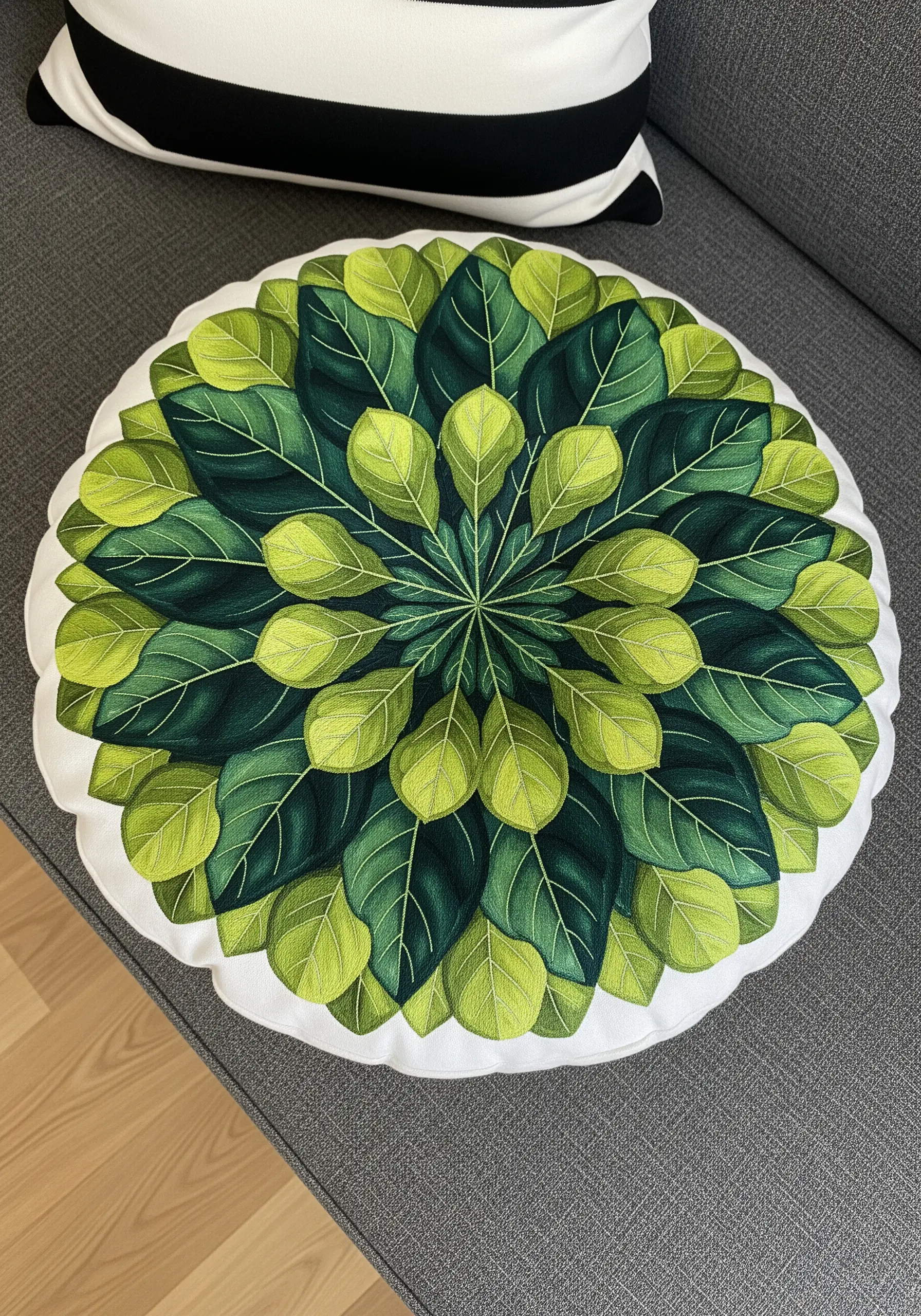 A round cushion with a radial pattern of embroidered leaves, transitioning from light to dark green.