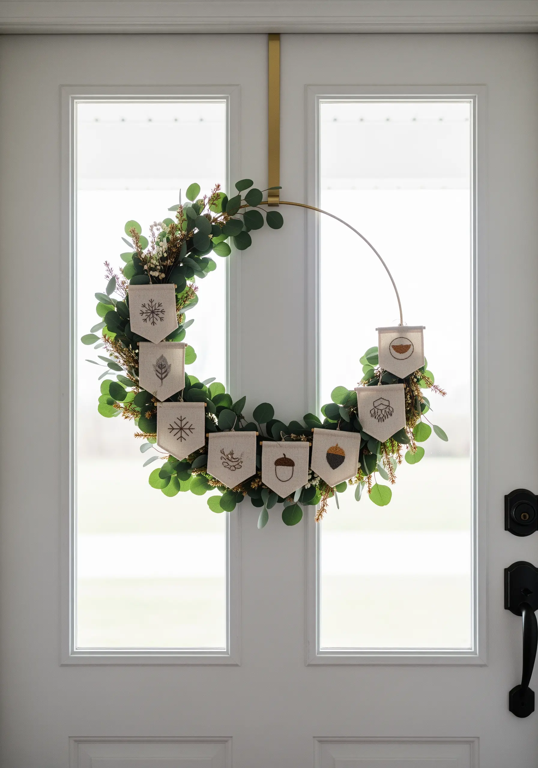 A modern wreath with eucalyptus and tiny embroidered banners featuring seasonal motifs like snowflakes and acorns.