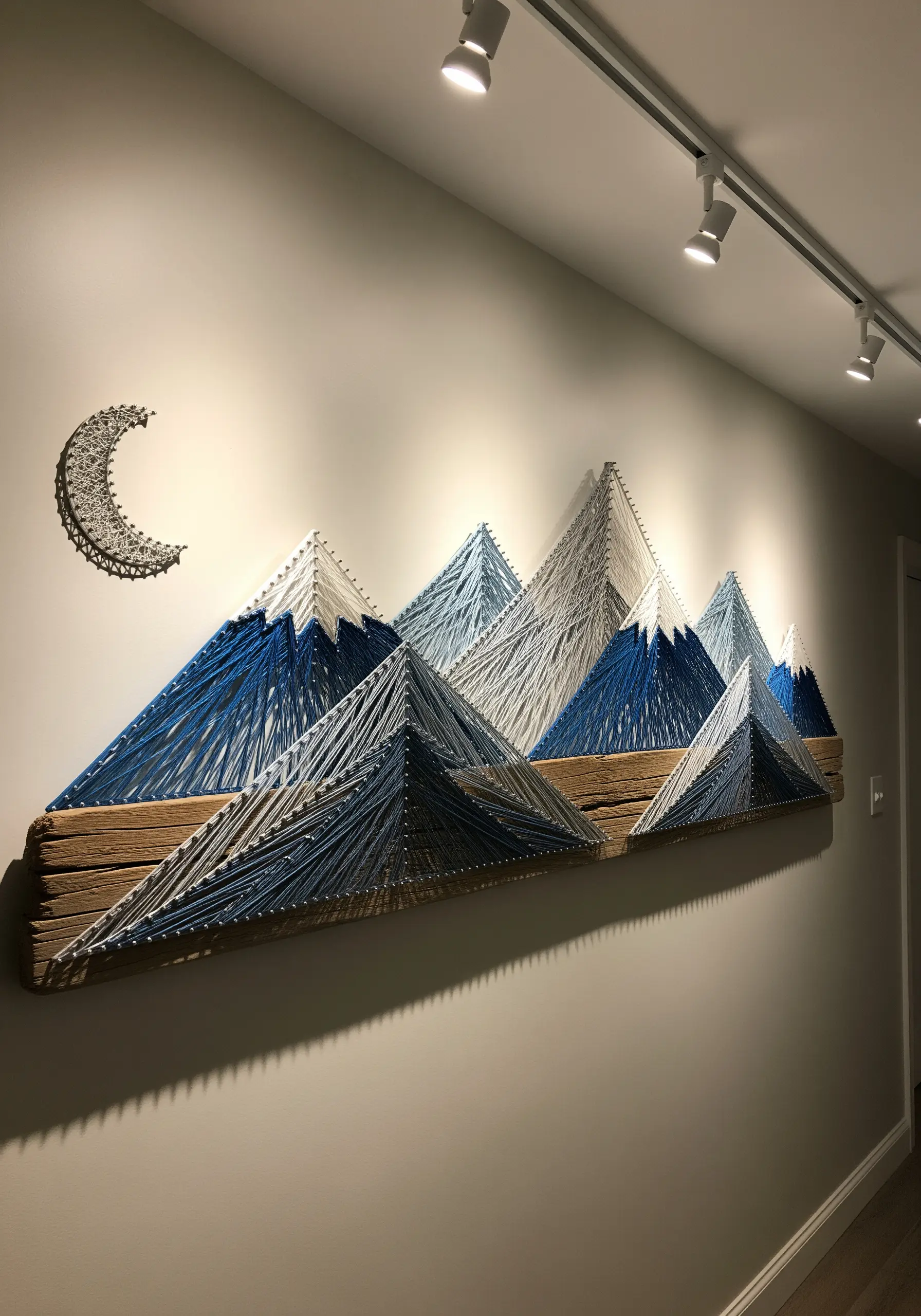 A large wall installation of string art mountains across multiple wood planks in shades of blue.