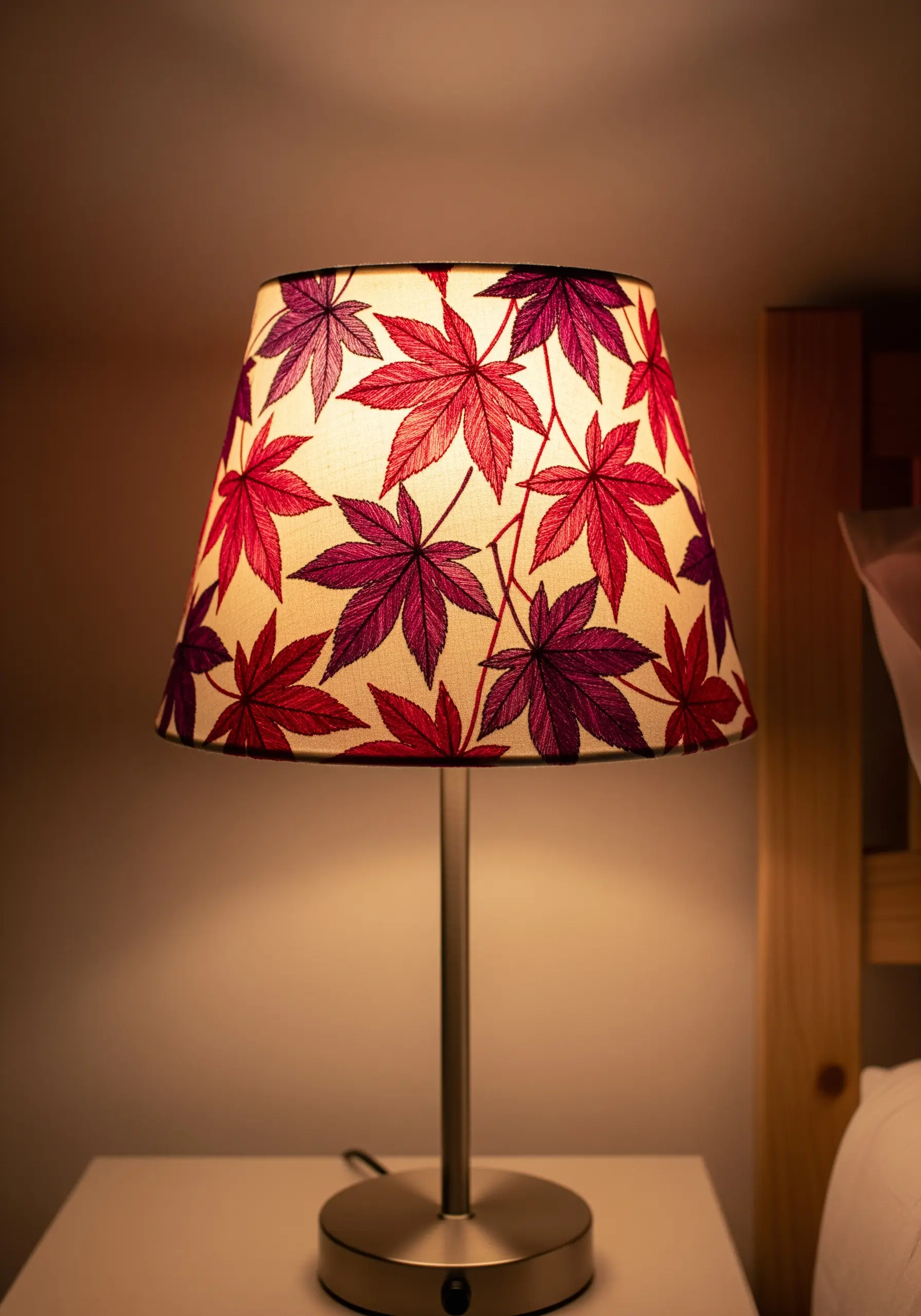 A lampshade with embroidered Japanese maple leaves in red and purple, glowing warmly.