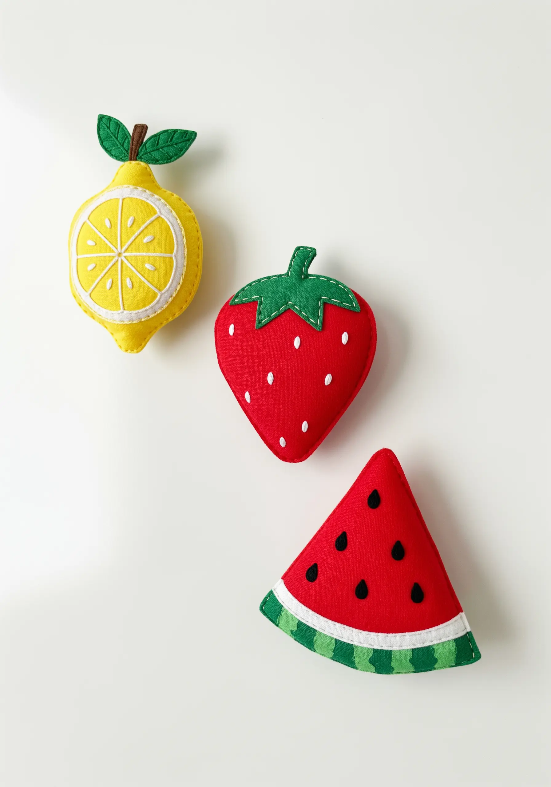 Three-dimensional felt fruits—a lemon, strawberry, and watermelon slice—with simple embroidered details.