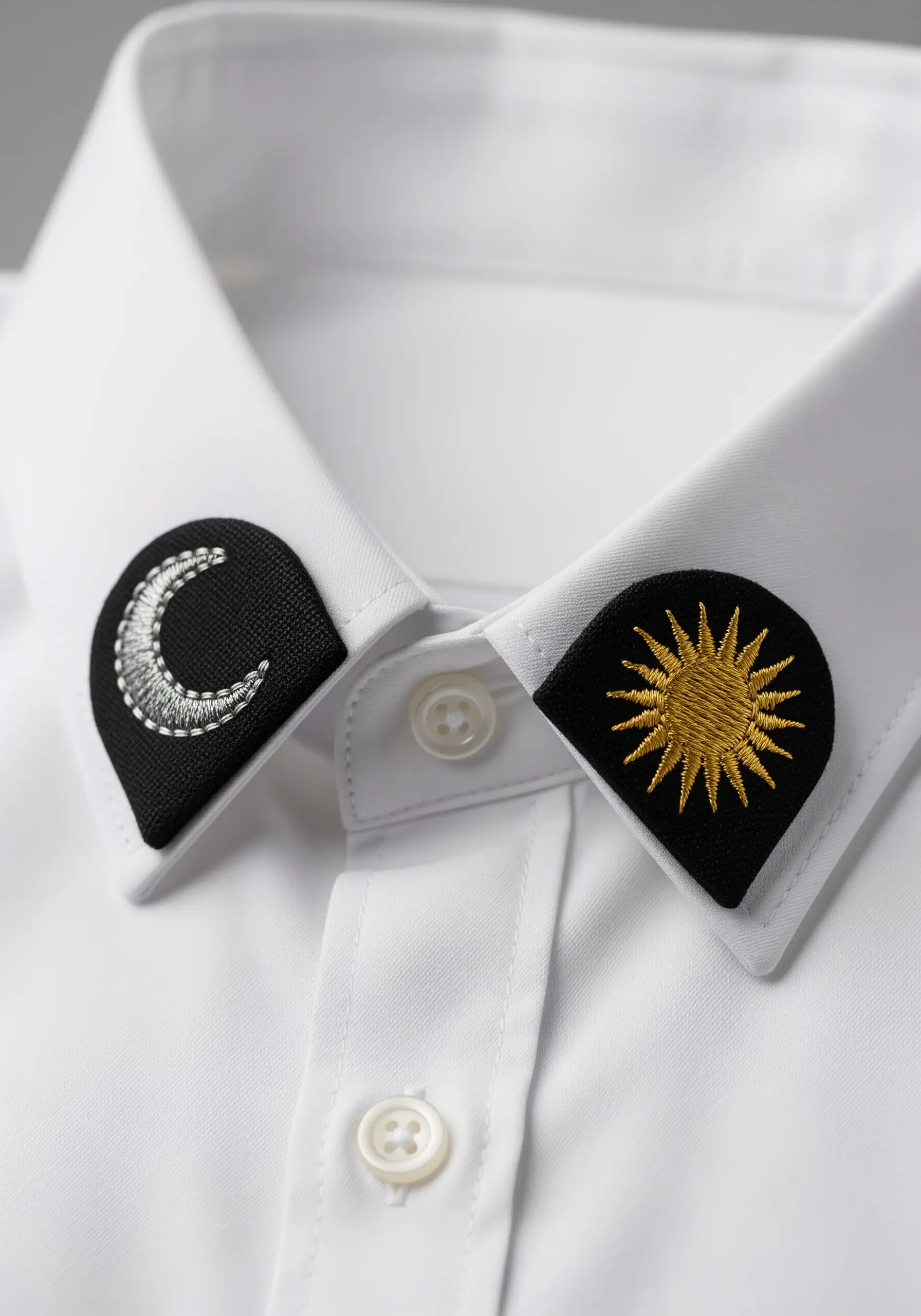 Embroidered sun and moon collar pins on a white button-down shirt.