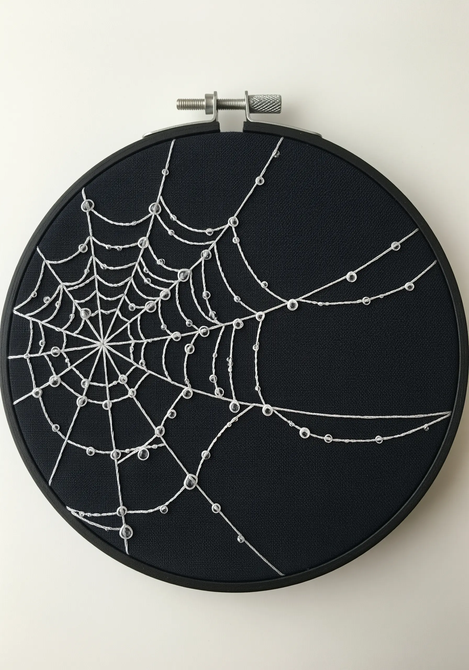 Minimalist embroidery of a spider web on black fabric with clear glass beads as dewdrops.