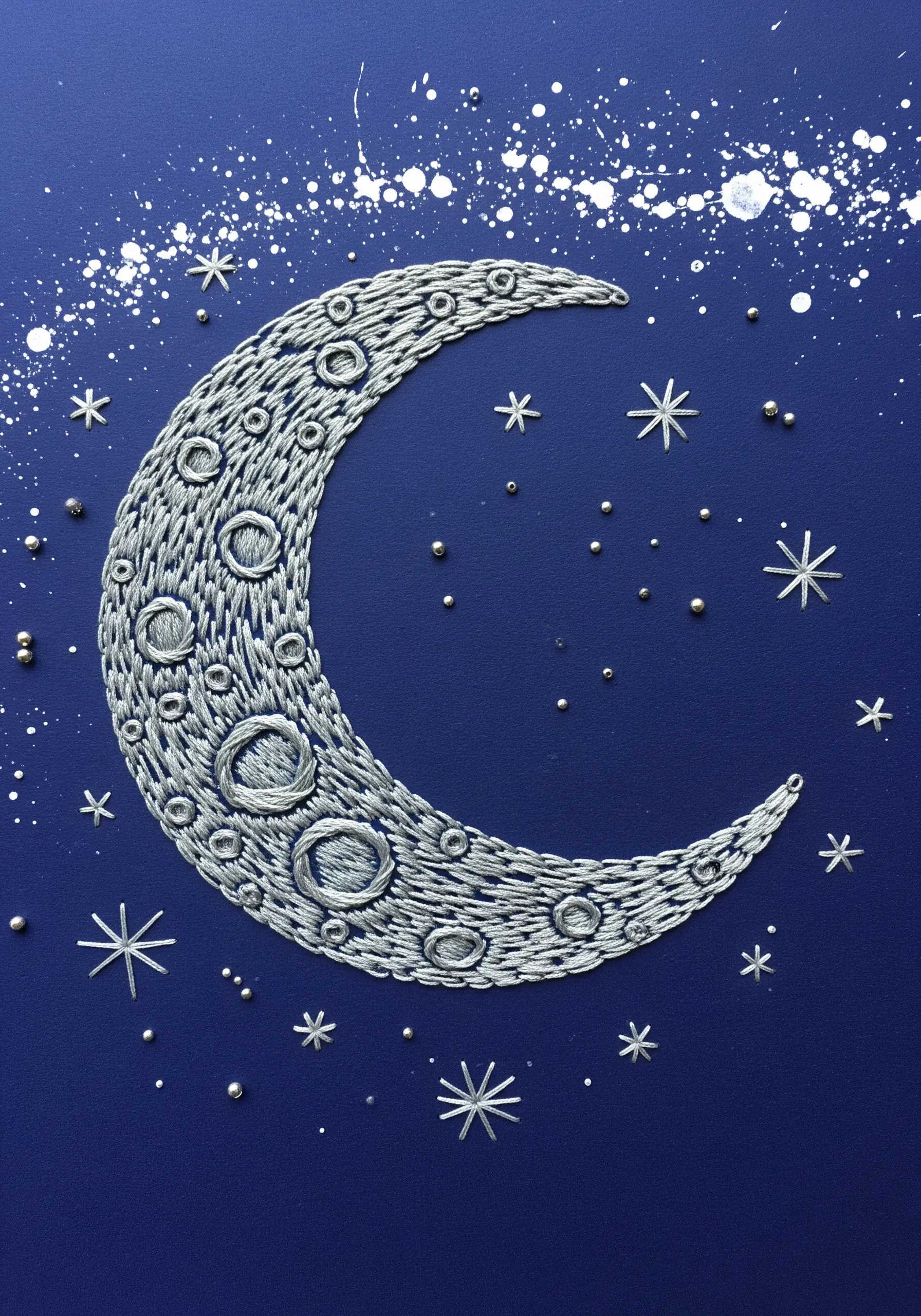 An embroidered crescent moon with textural fill stitching and metallic details on a dark background