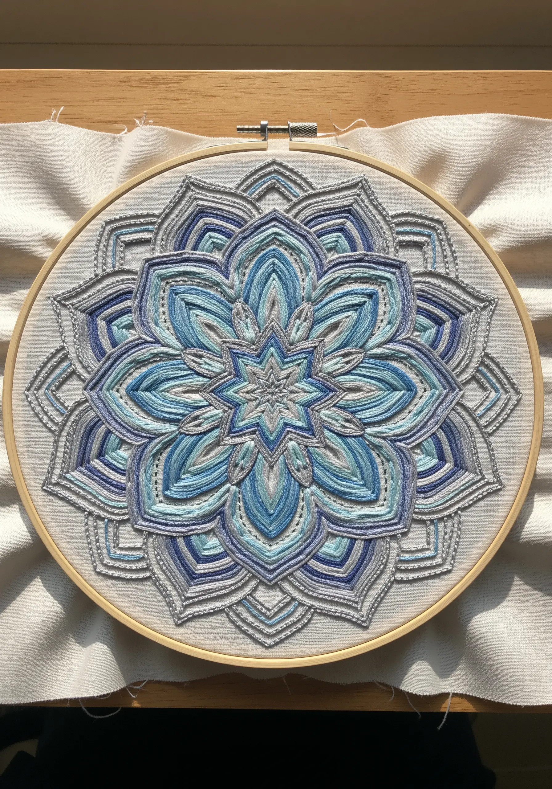 Intricate embroidered mandala with variegated blue, white, and gray threads.