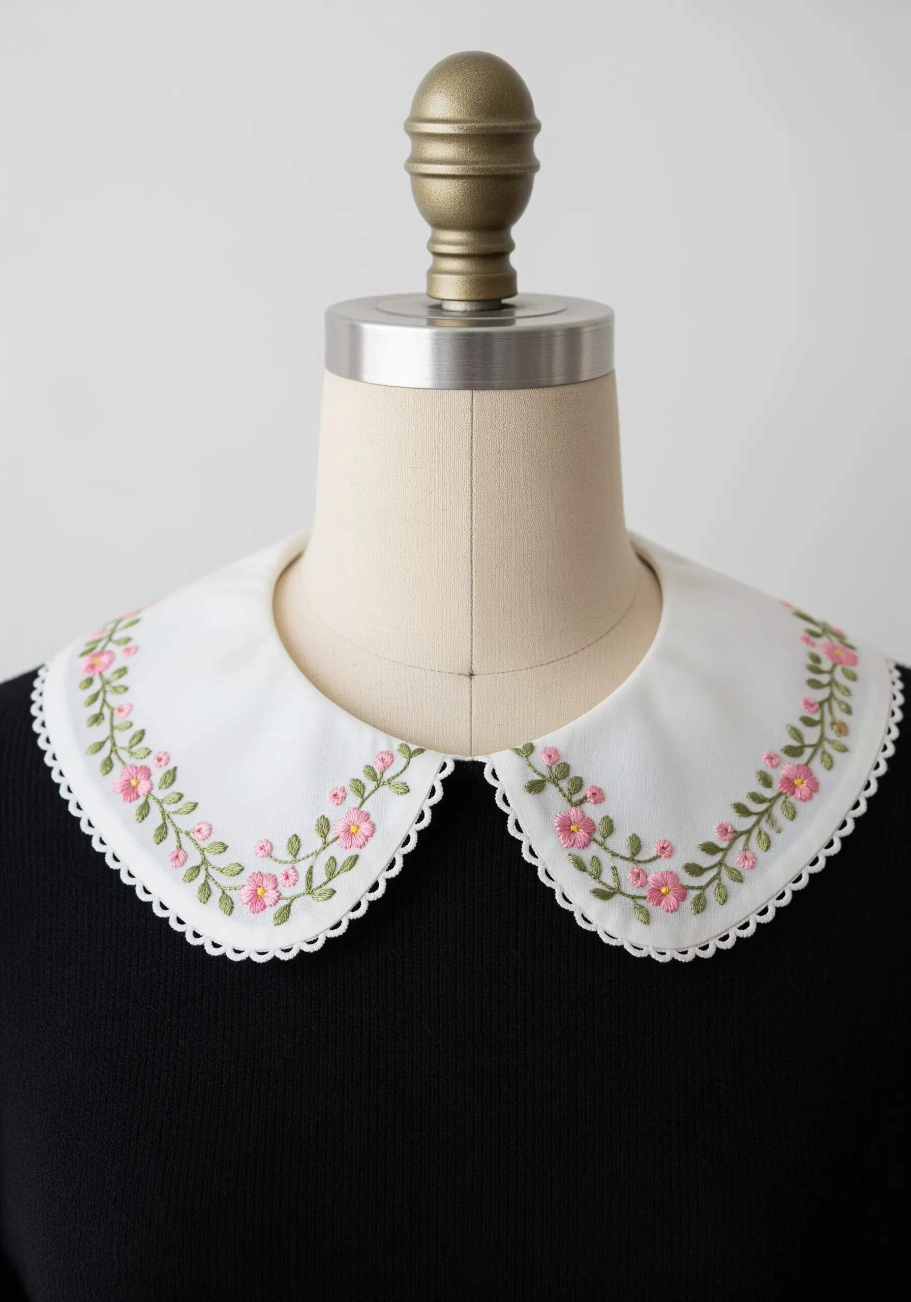 Dainty pink flowers and green vines embroidered along the edge of a white collar.