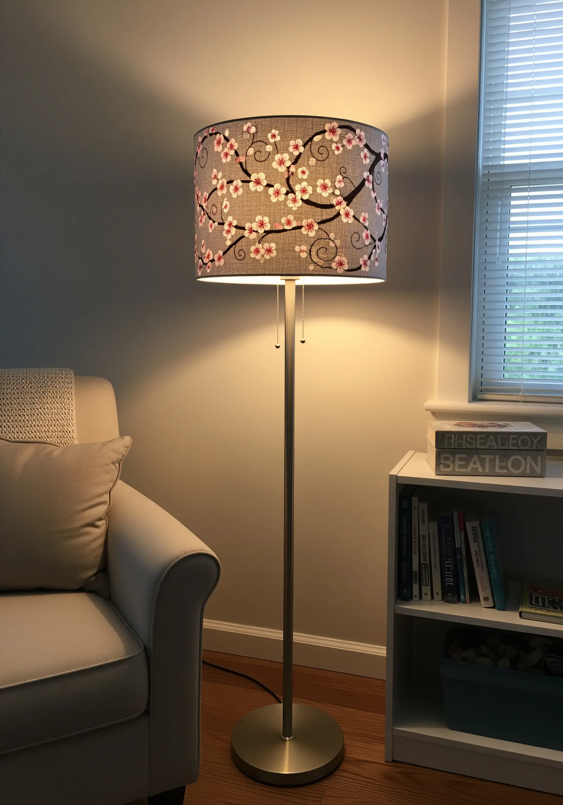 A gray fabric lampshade embroidered with a pattern of cherry blossoms and swirling branches.