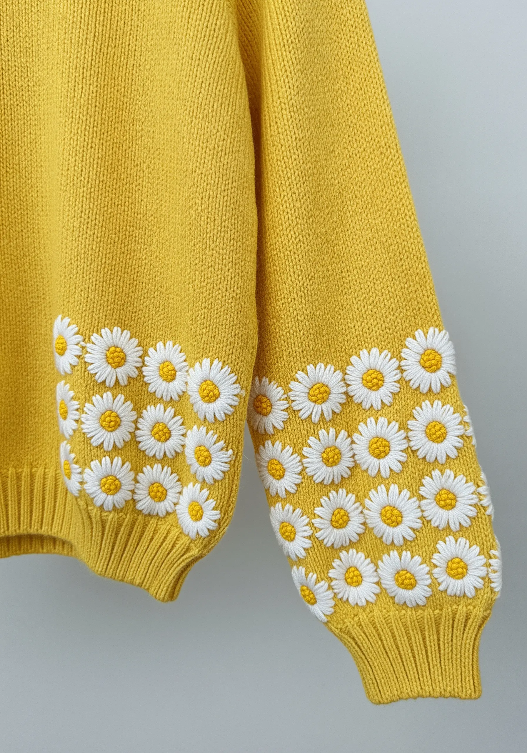 Densely embroidered daisy chain border around the cuffs of a yellow sweater.