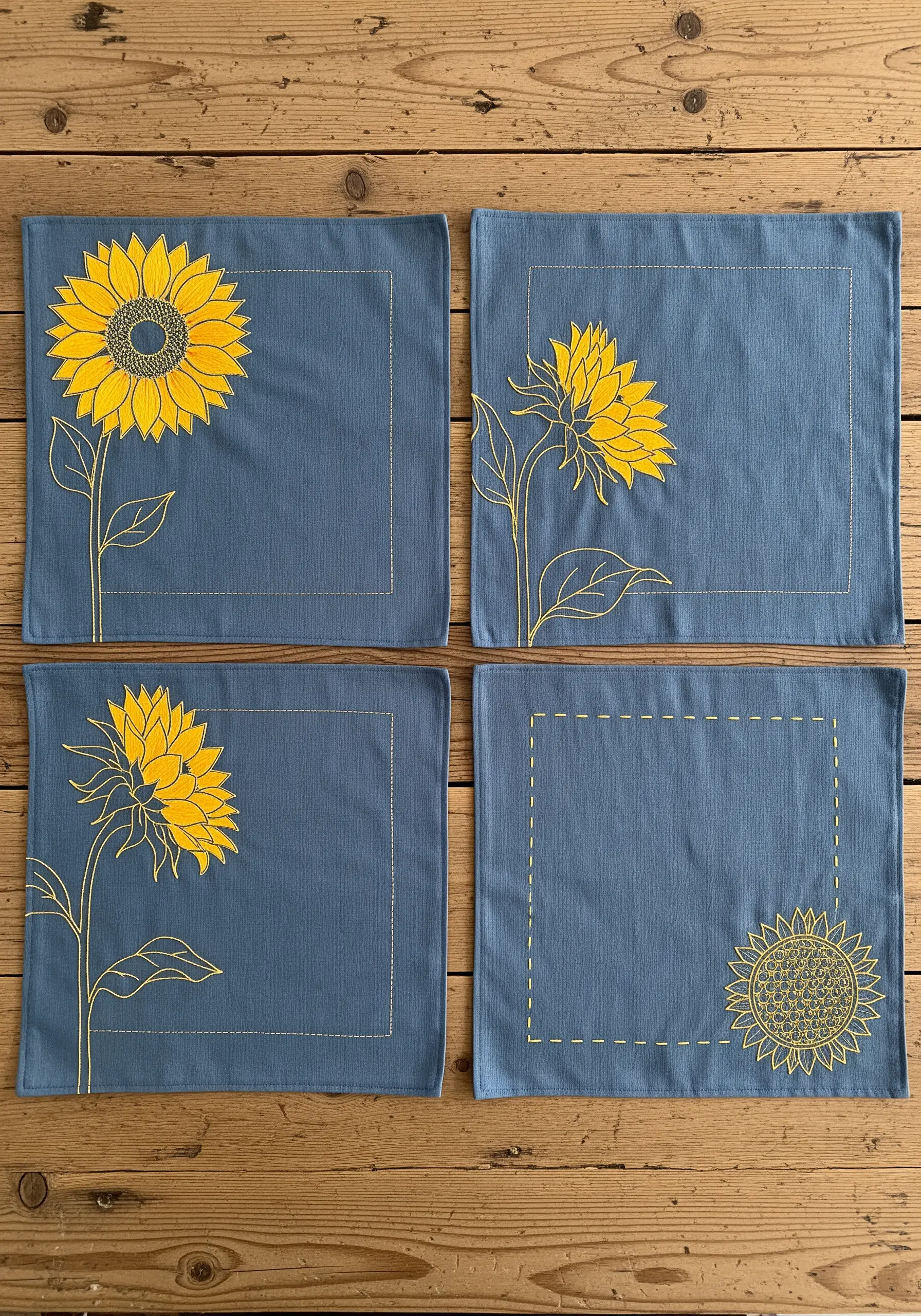 Set of four blue placemats with minimalist sunflower line art embroidery in yellow thread.