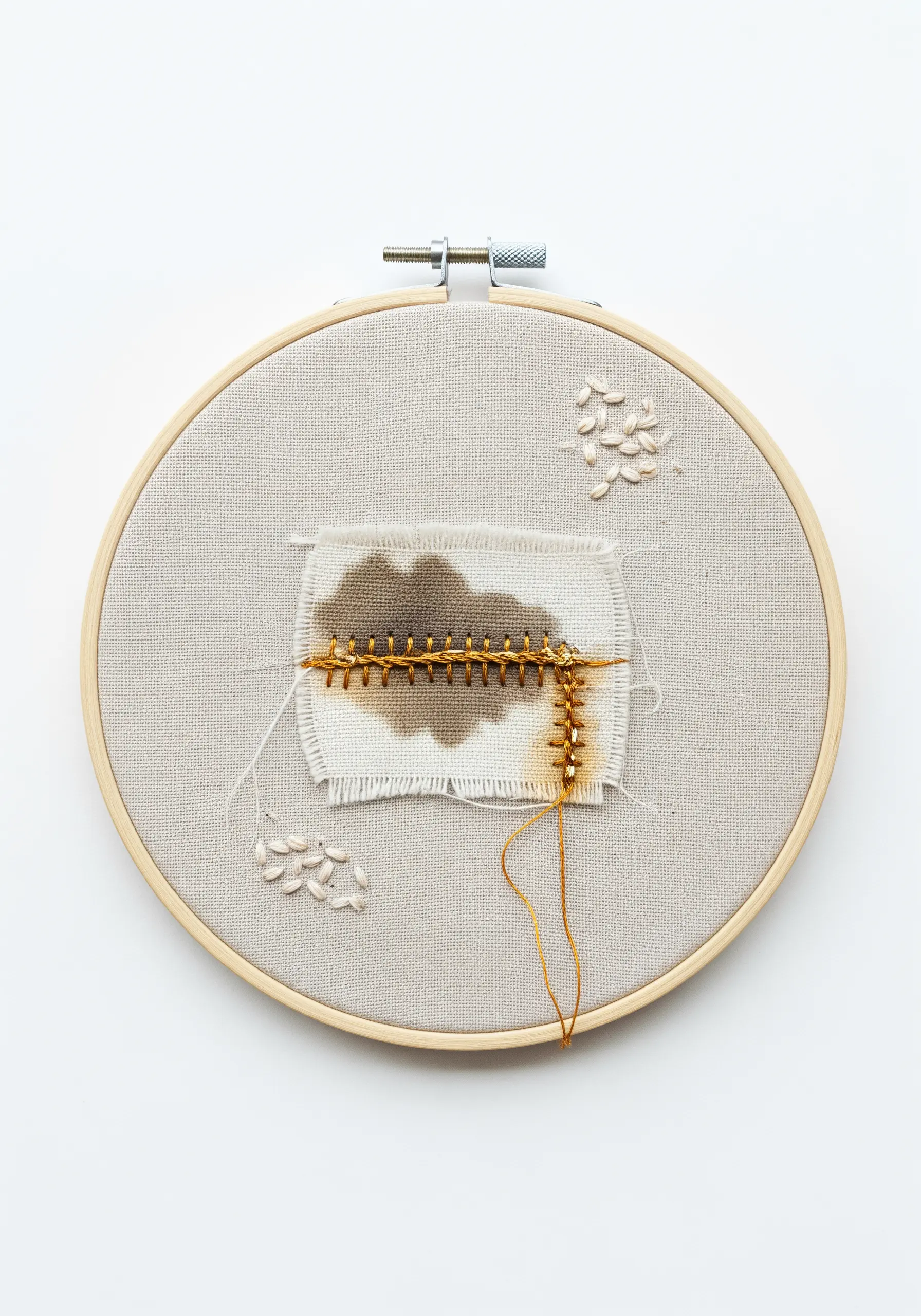 Minimalist embroidery with a coffee-stained fabric scrap repaired with a gold blanket stitch.