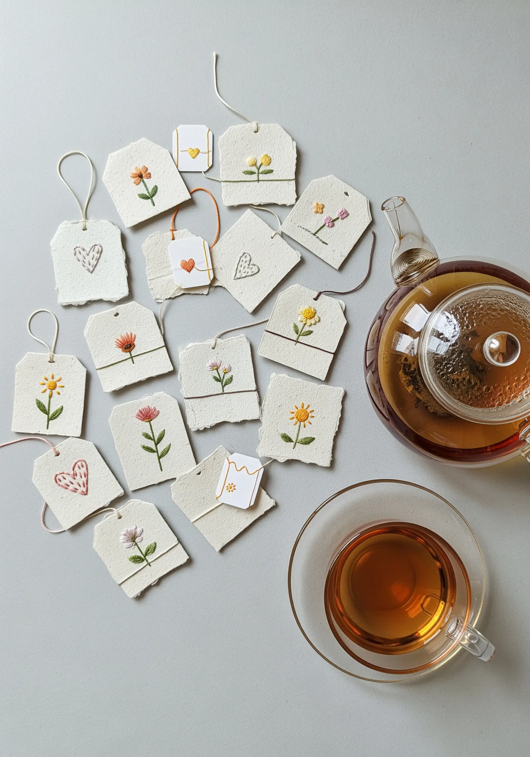 A collection of tiny handmade paper tags, each embroidered with a single, simple floral motif.