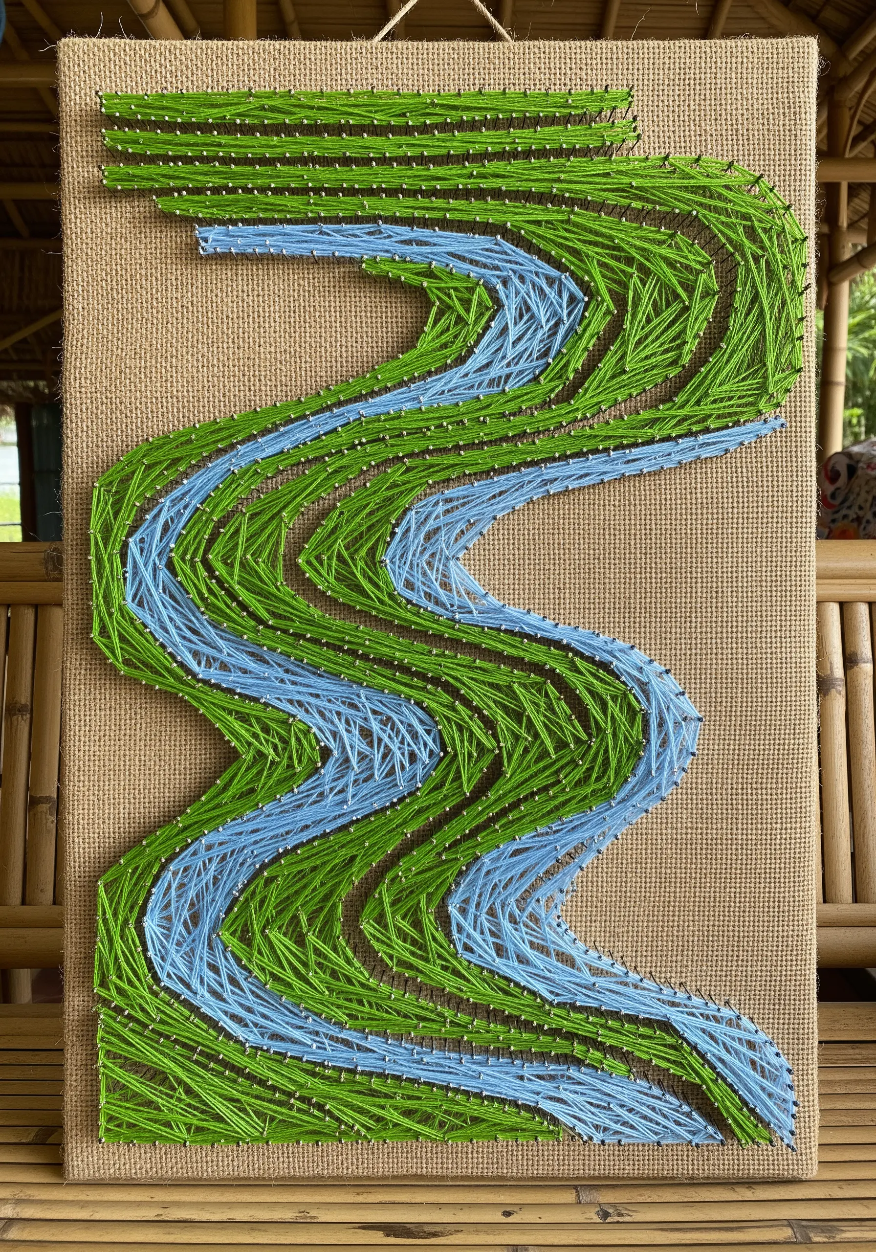 String art of a winding blue and green river on a coarse, natural burlap canvas.