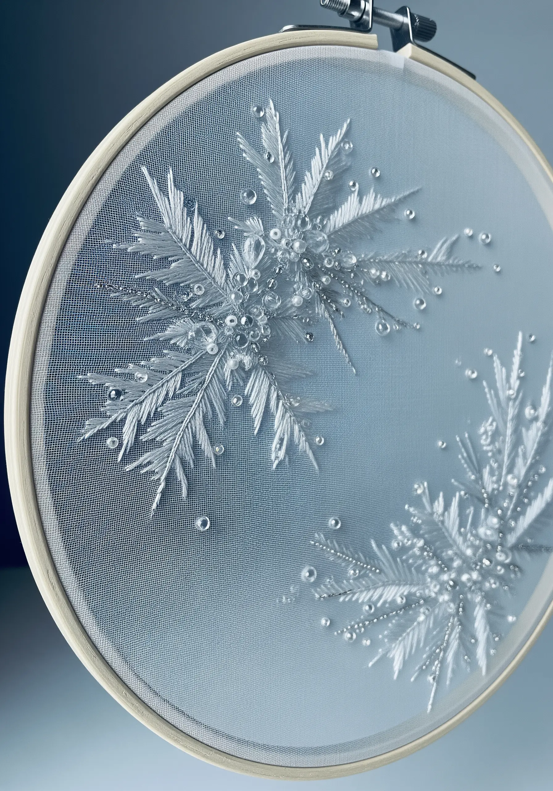 Delicate white embroidery of a snowflake with clear beads on a sheer tulle fabric.