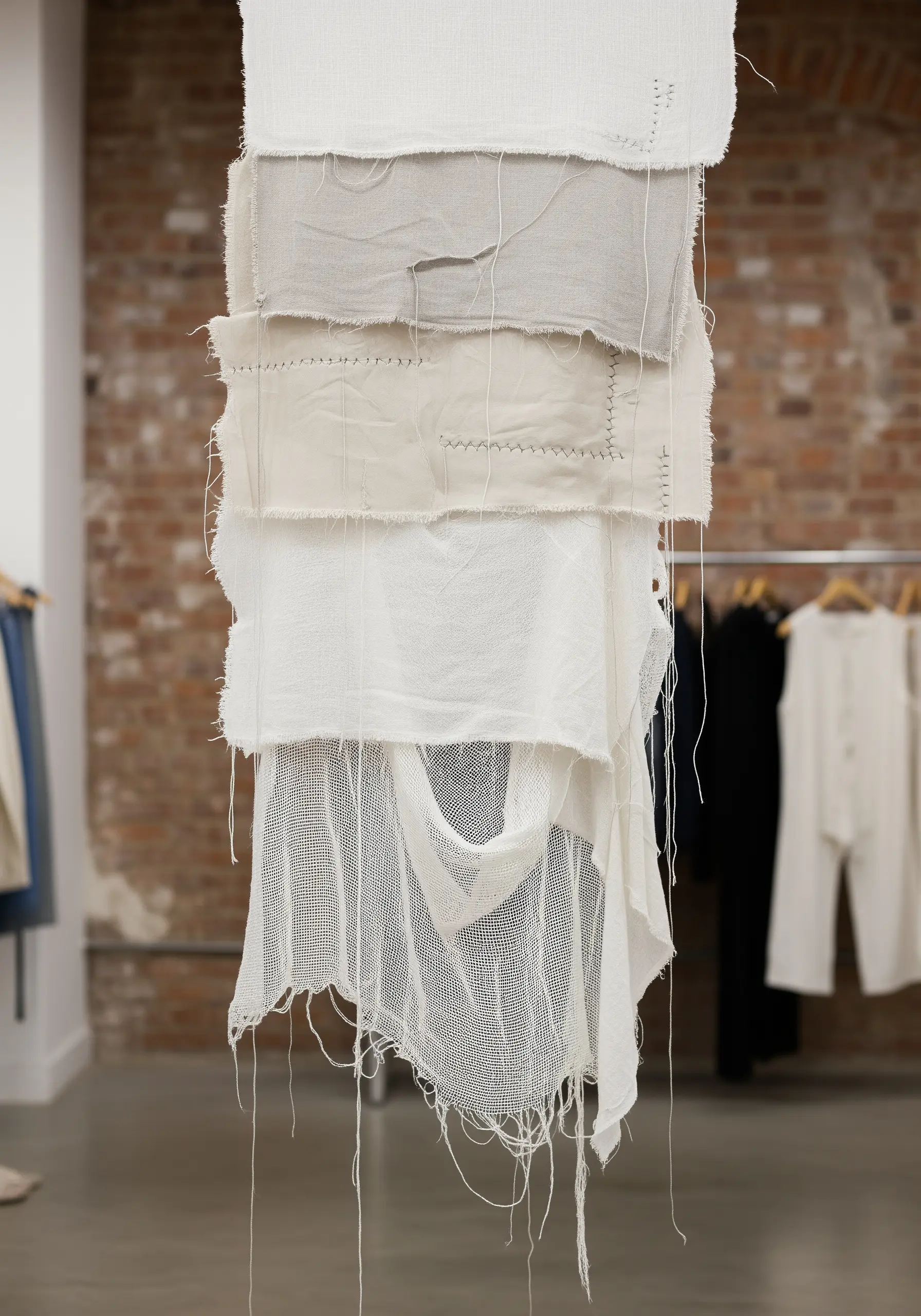A hanging textile piece made of layered white and off-white fabric scraps with visible stitches.