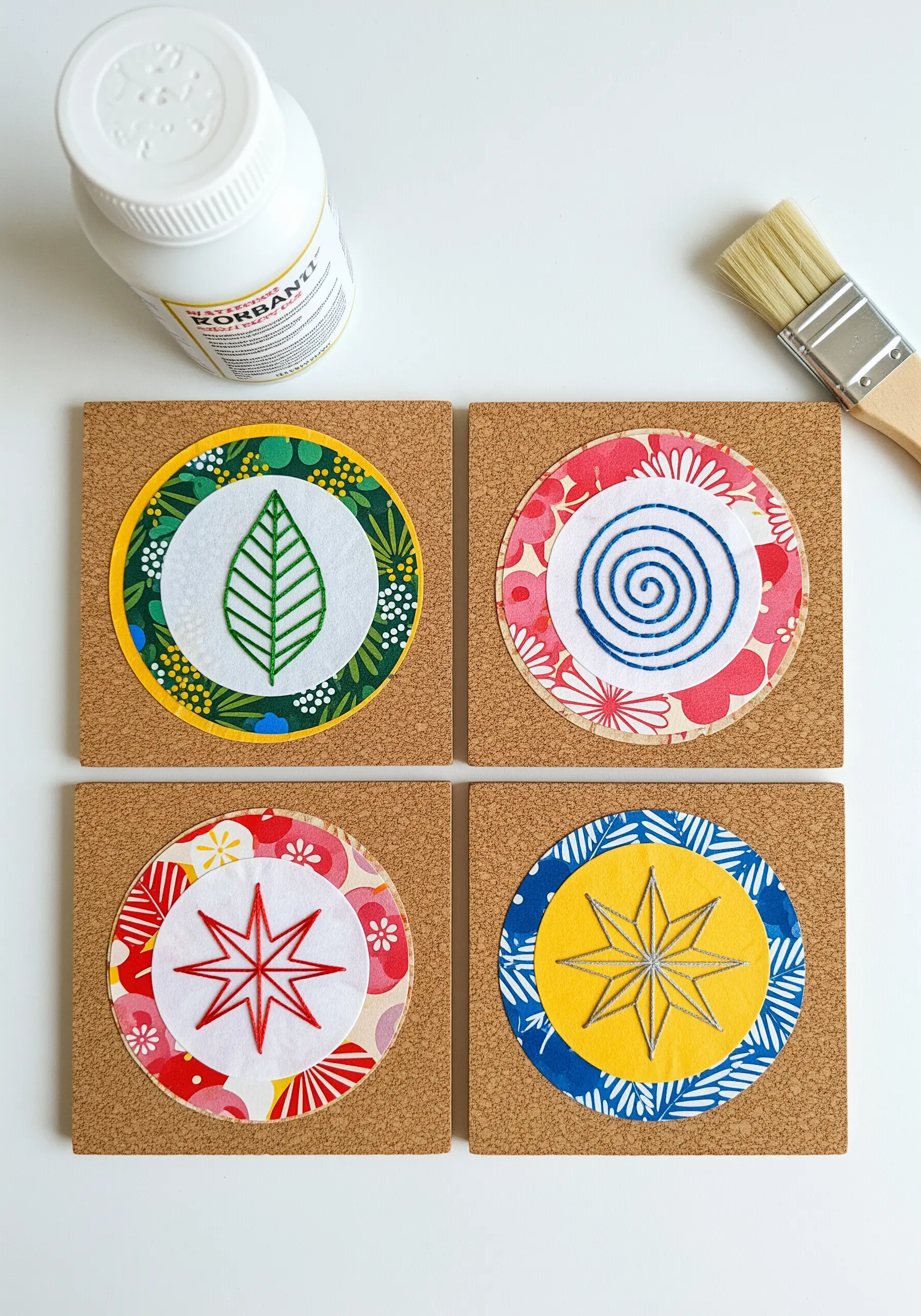 Four handmade coasters combining embroidered felt circles with patterned fabric on cork bases