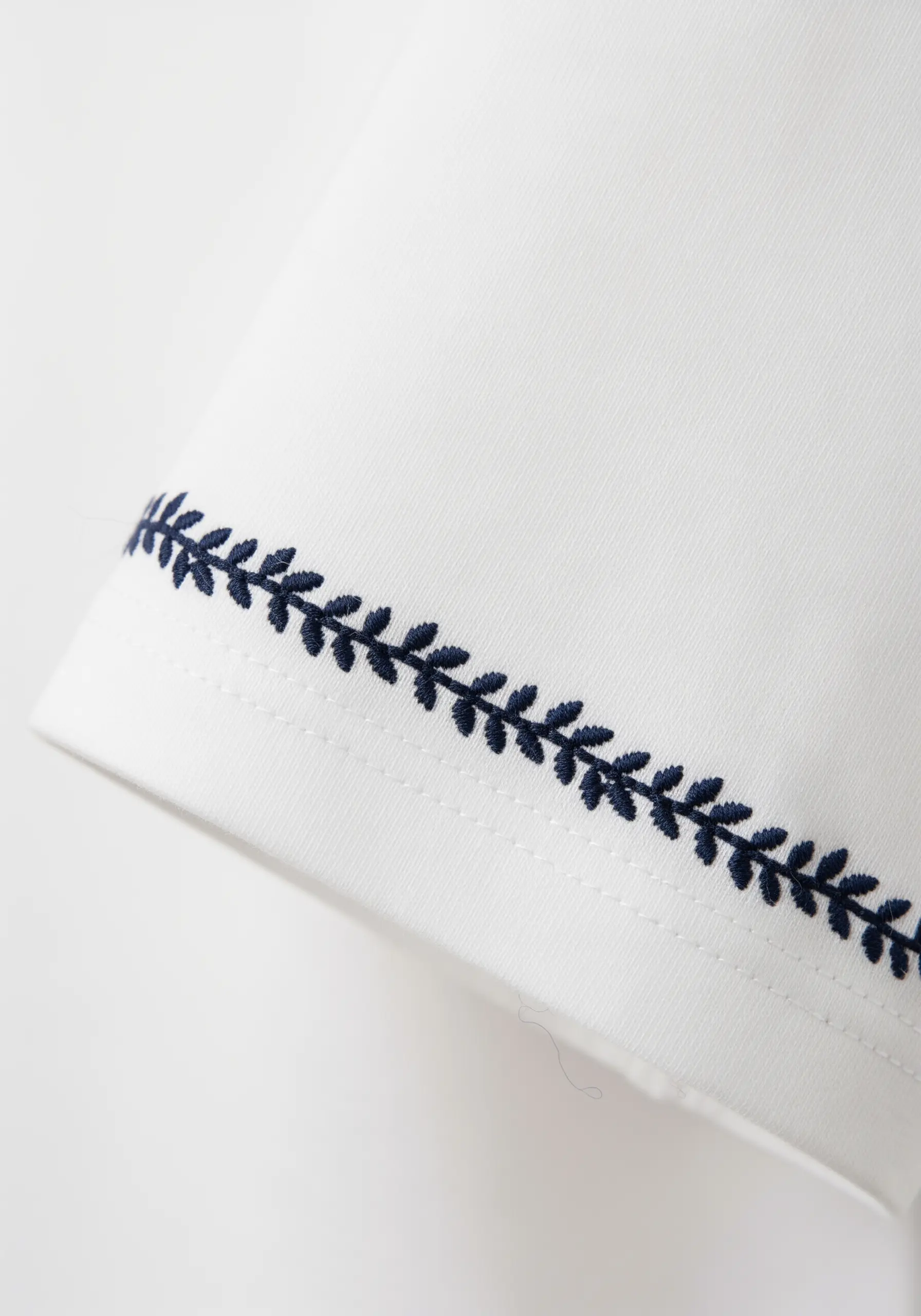 A simple navy blue fern stitch border embroidered around a t-shirt sleeve hem.