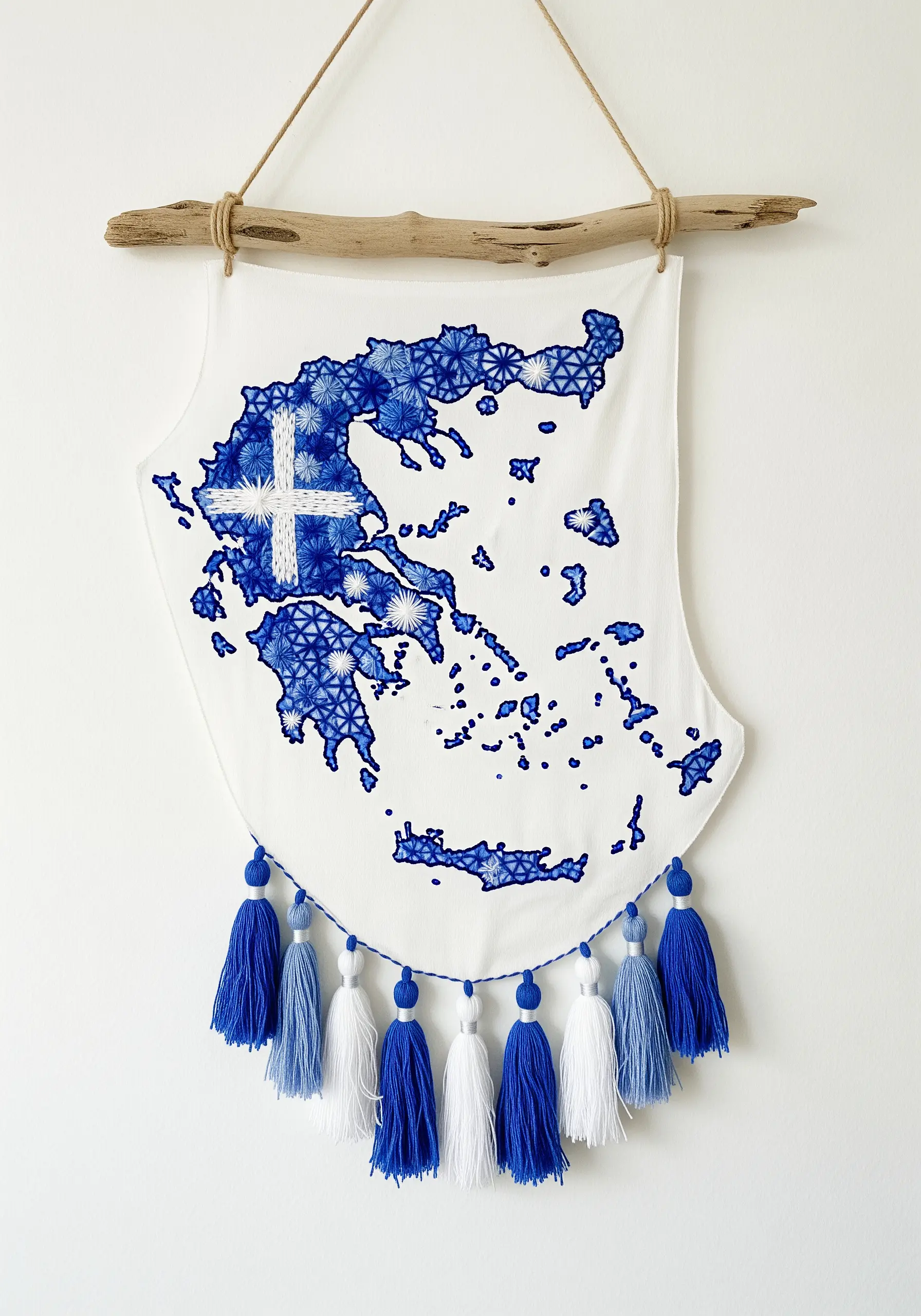 Embroidered map of Greece on a white banner, hung from driftwood with blue and white tassels.