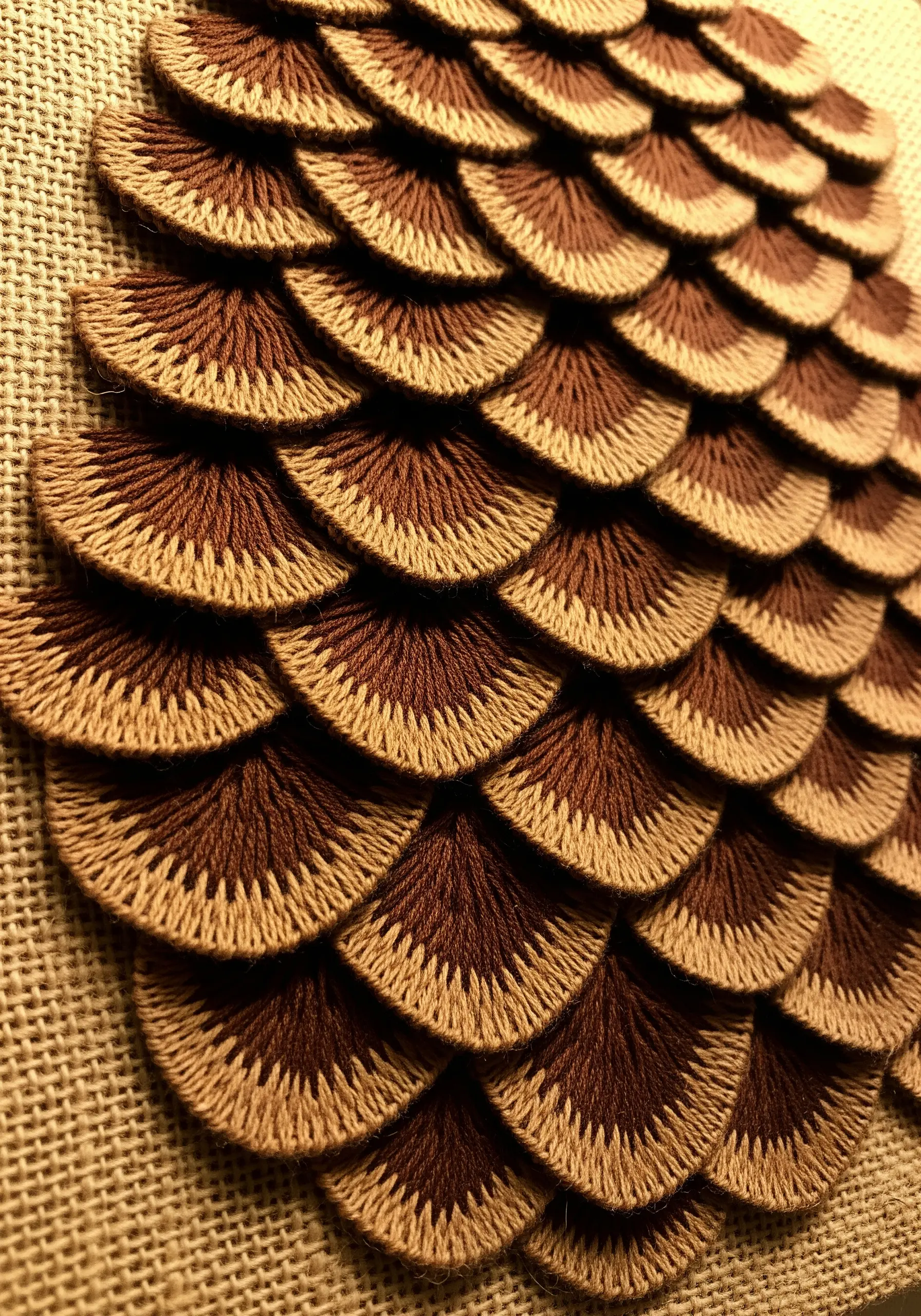 Close-up of layered satin stitch embroidery forming dimensional, two-toned pinecone scales.