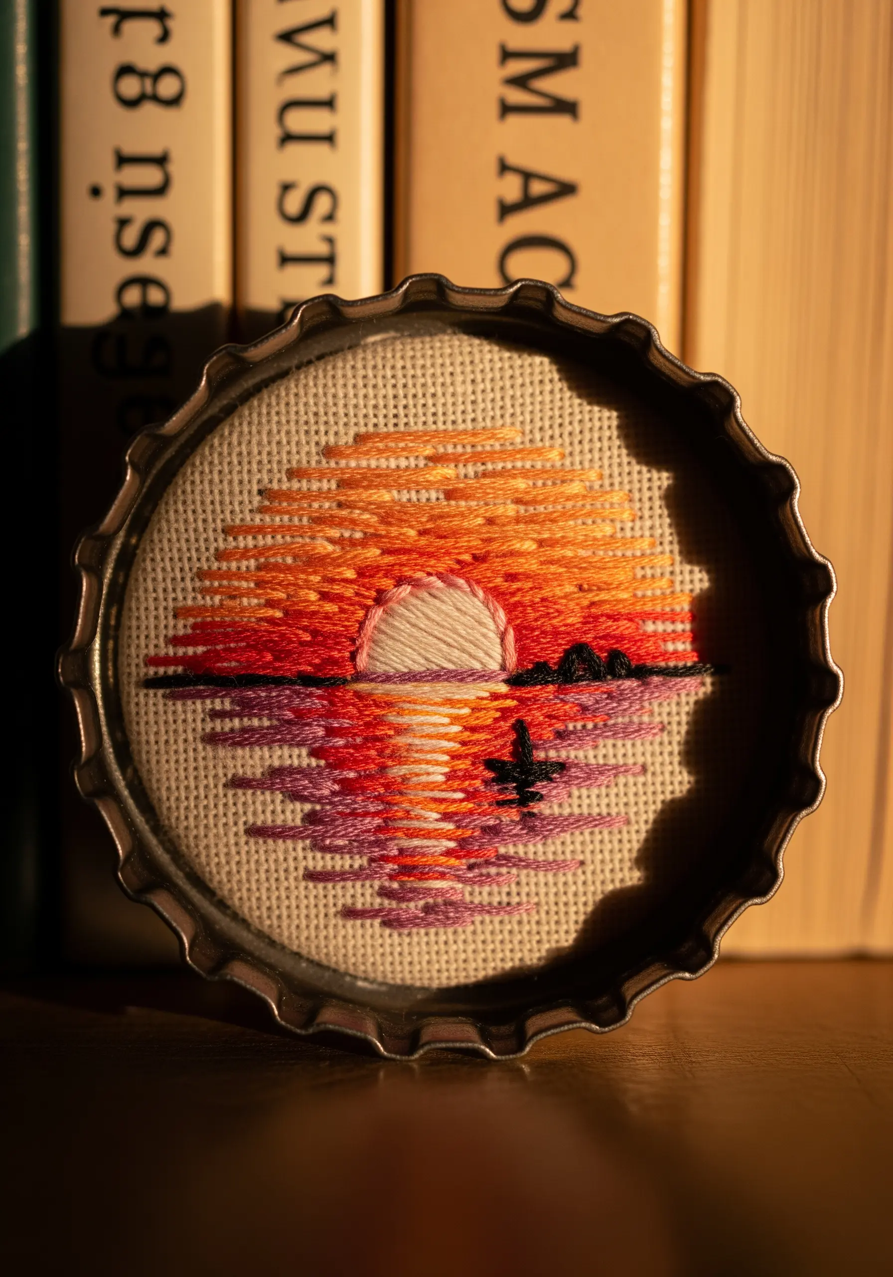 A miniature sunset landscape embroidered inside a metal bottle cap.