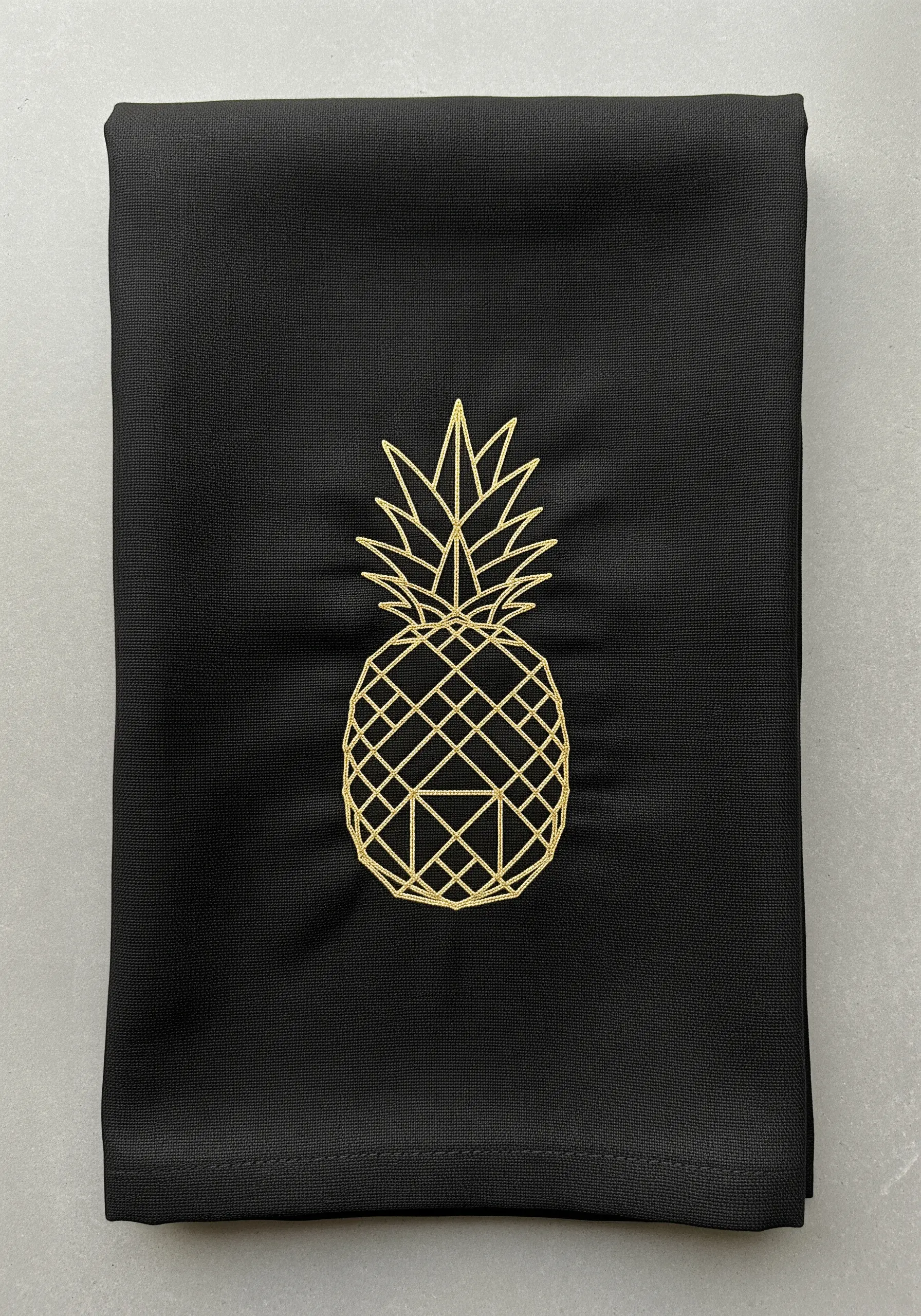 A geometric pineapple embroidered in gold metallic thread on a black napkin.