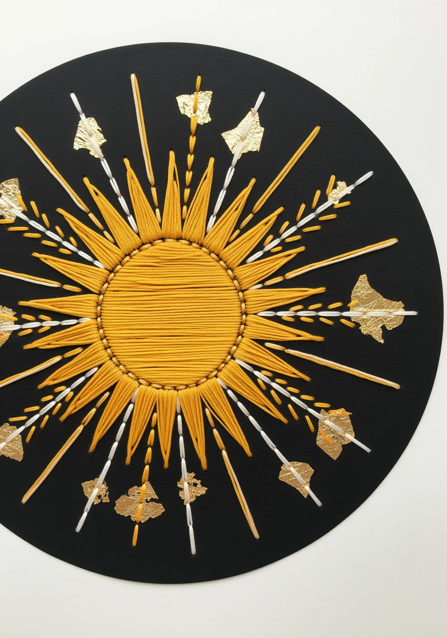 Embroidered sunburst on black paper with gold leaf flakes accenting the thread rays