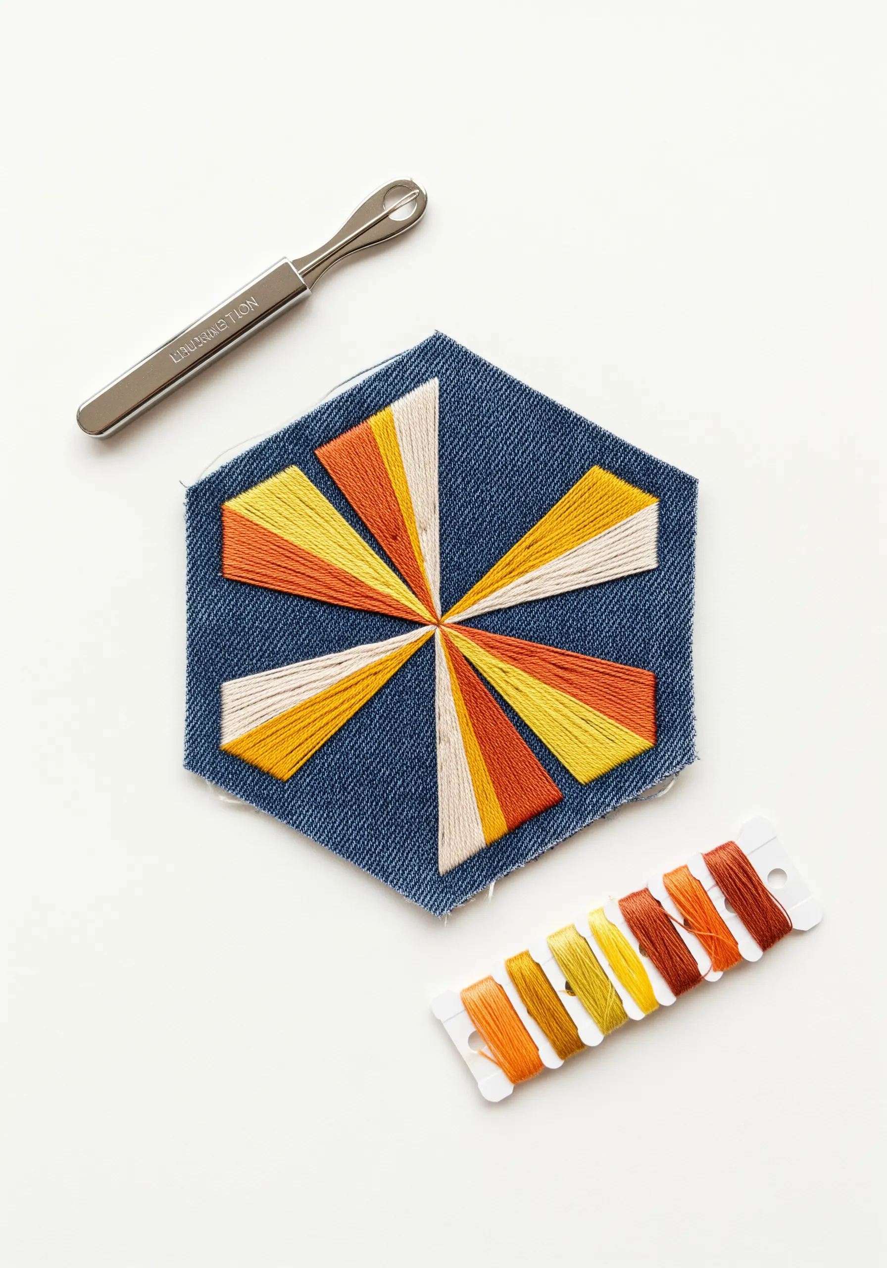 Geometric starburst pattern in yellow and orange satin stitch on a hexagonal denim scrap.