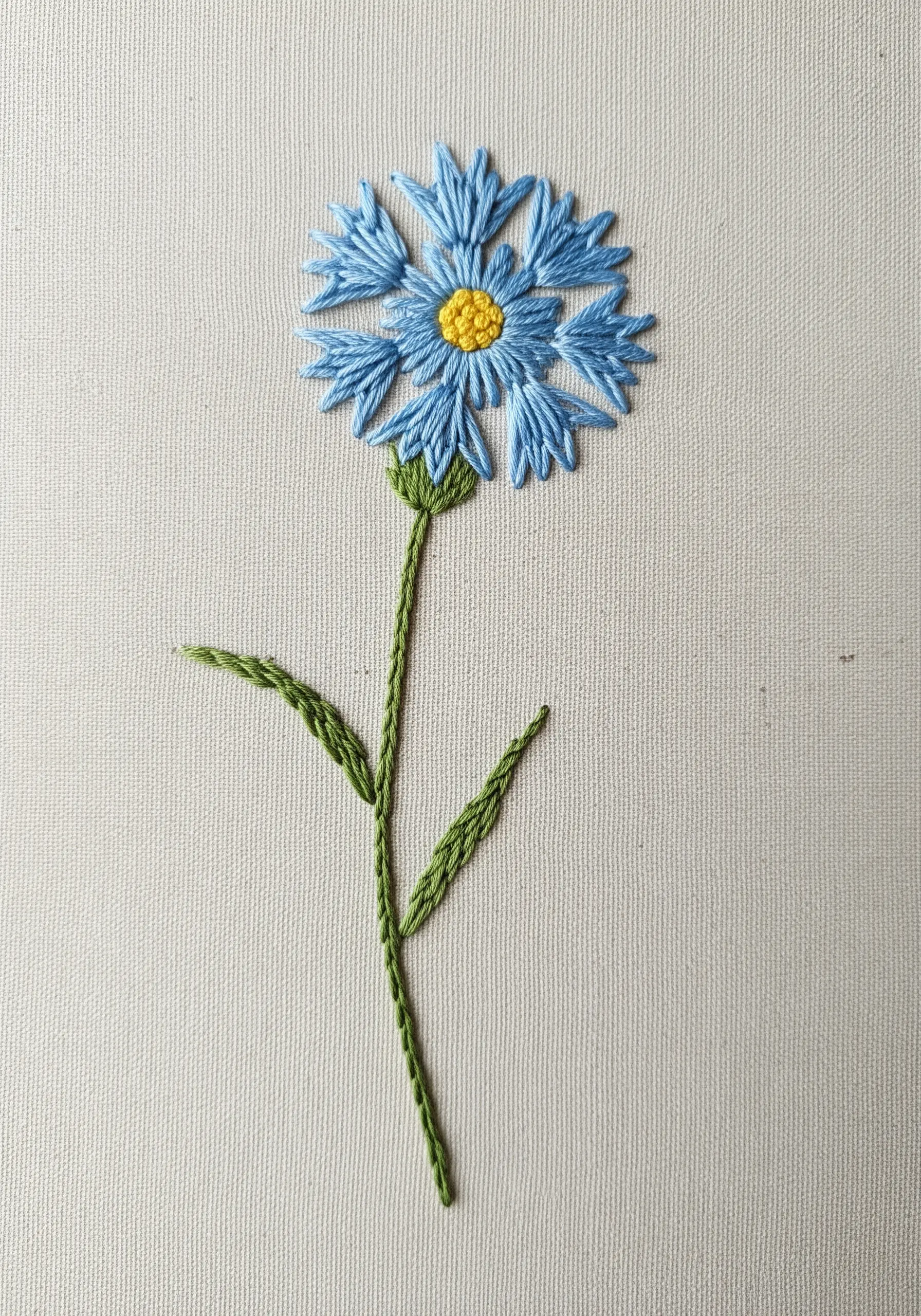 Stylized blue flower with detached chain stitch petals and a yellow French knot center.