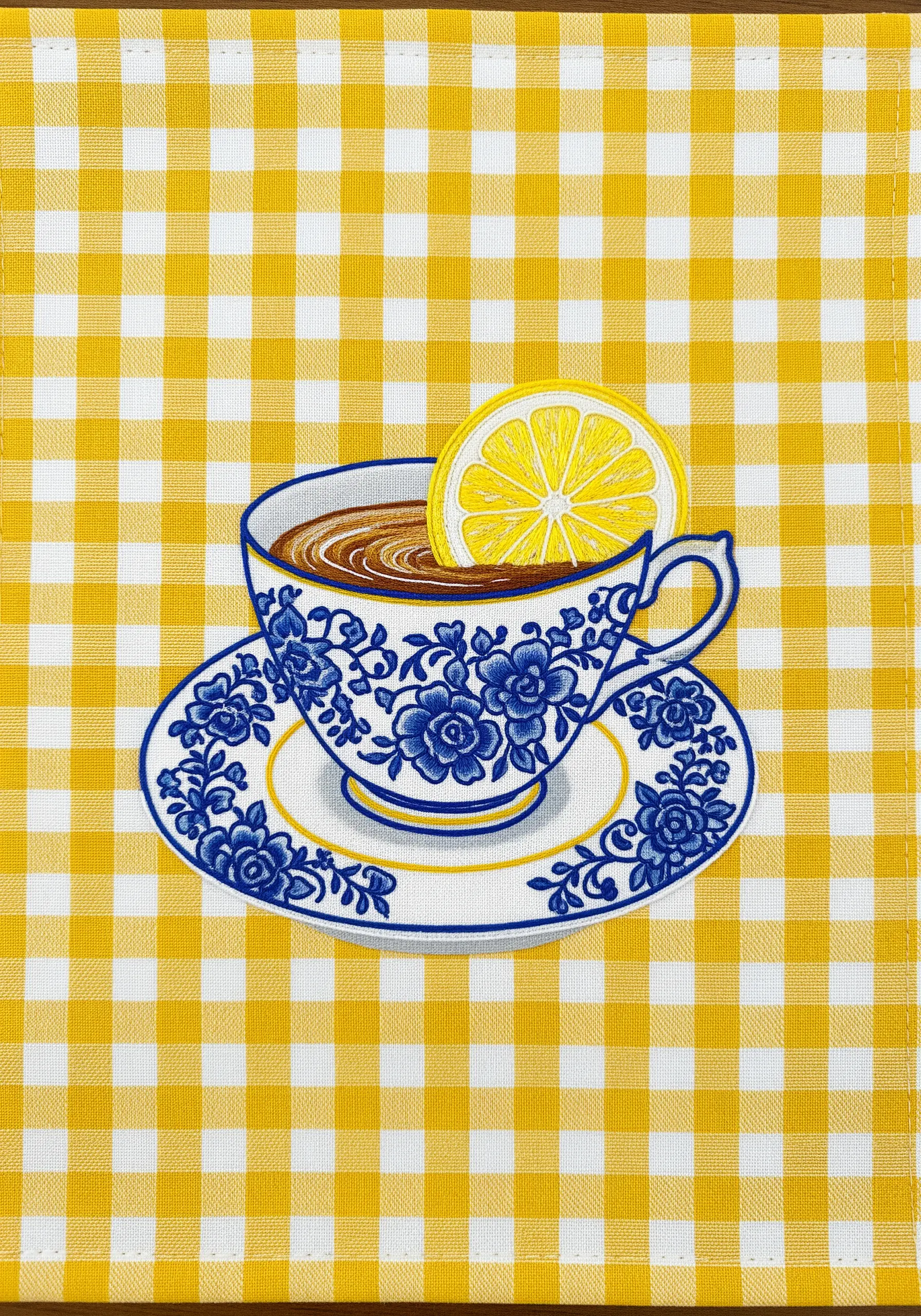 An embroidered blue and white teacup stitched onto a yellow gingham placemat.