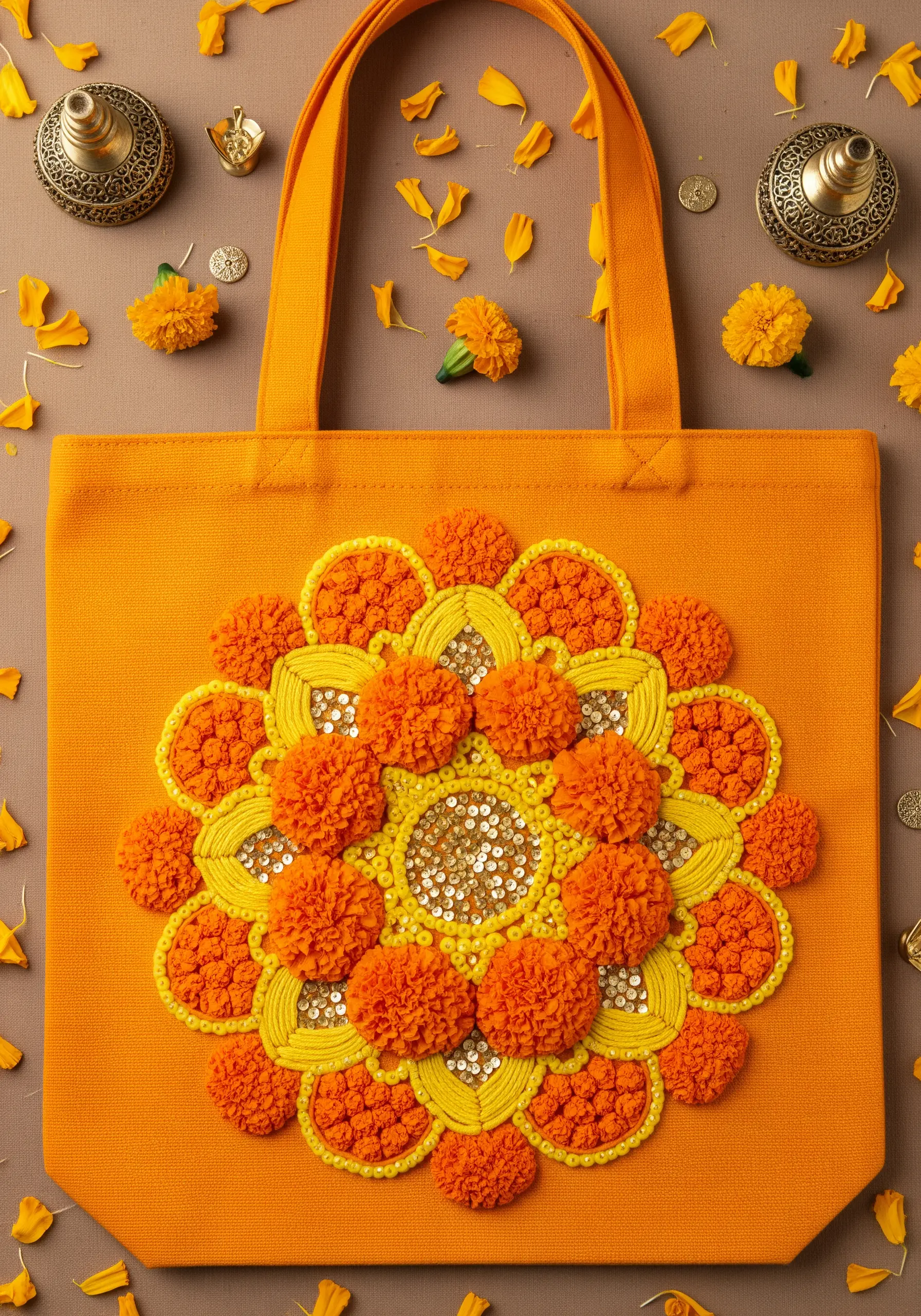 A vibrant marigold mandala on an orange tote bag, featuring French knots and a sequin center.