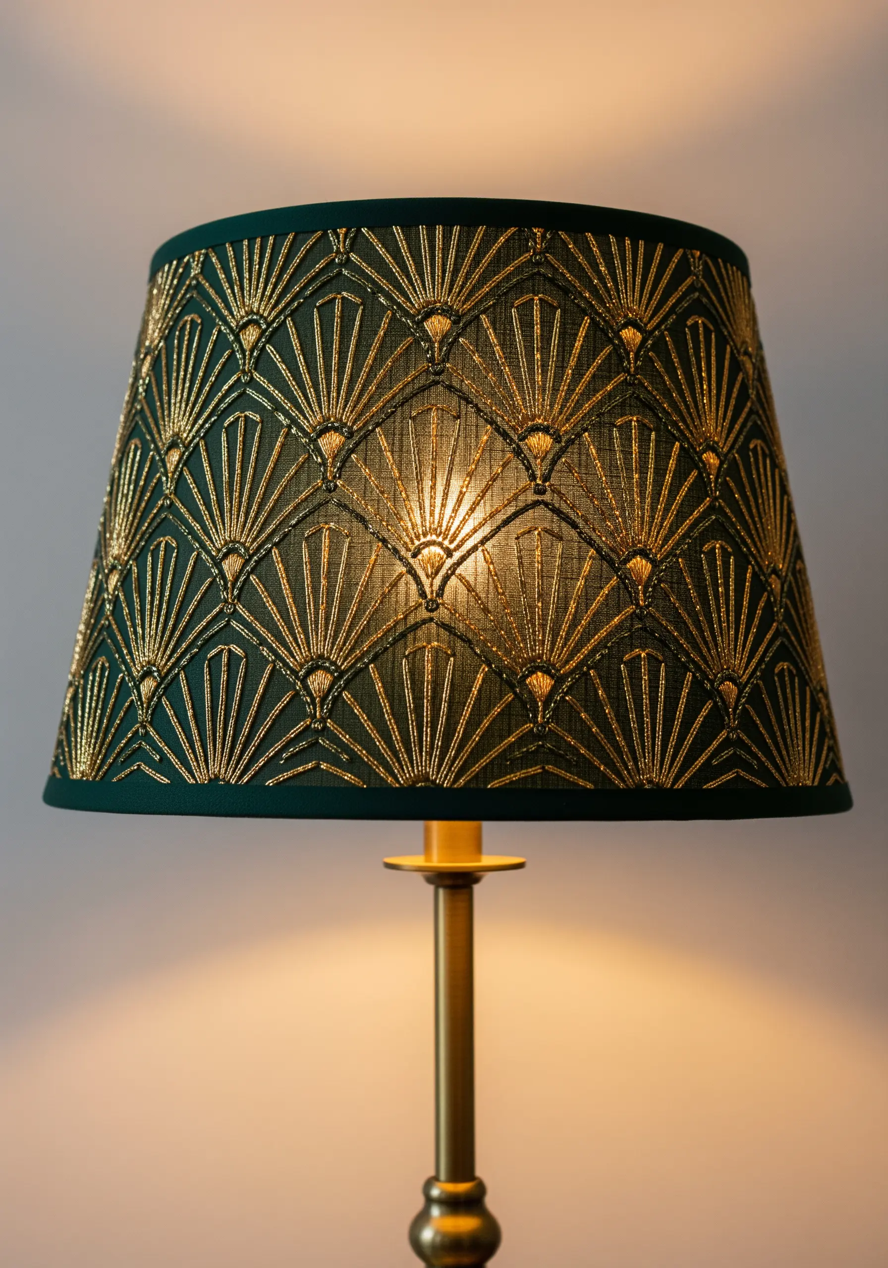 A dark green lampshade with a gold-embroidered Art Deco fan pattern, illuminated from within.