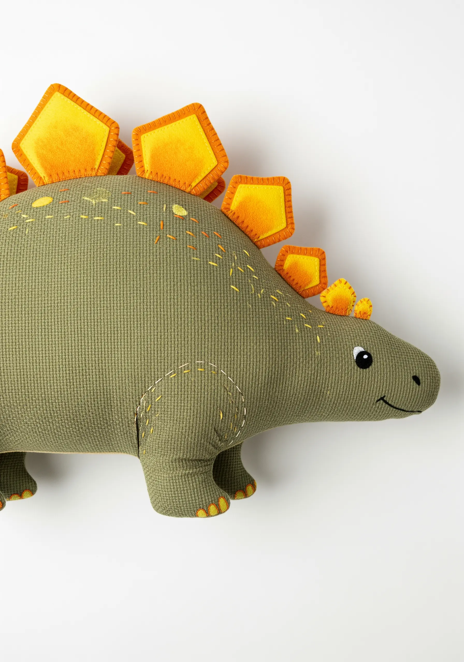 A shaped dinosaur pillow with 3D felt plates stitched along its back.