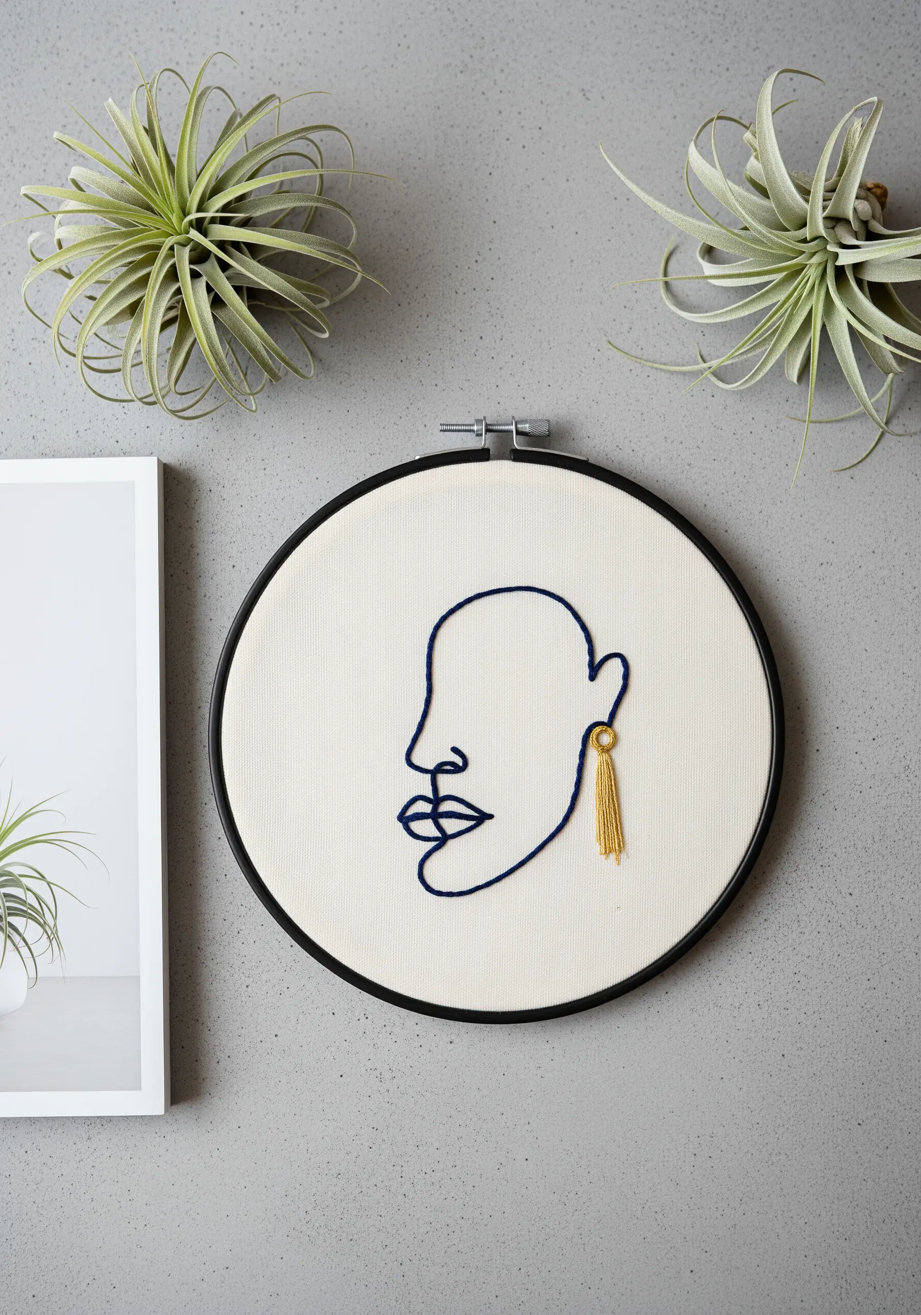 Embroidered line art face with a real gold tassel earring dangling from the earlobe.
