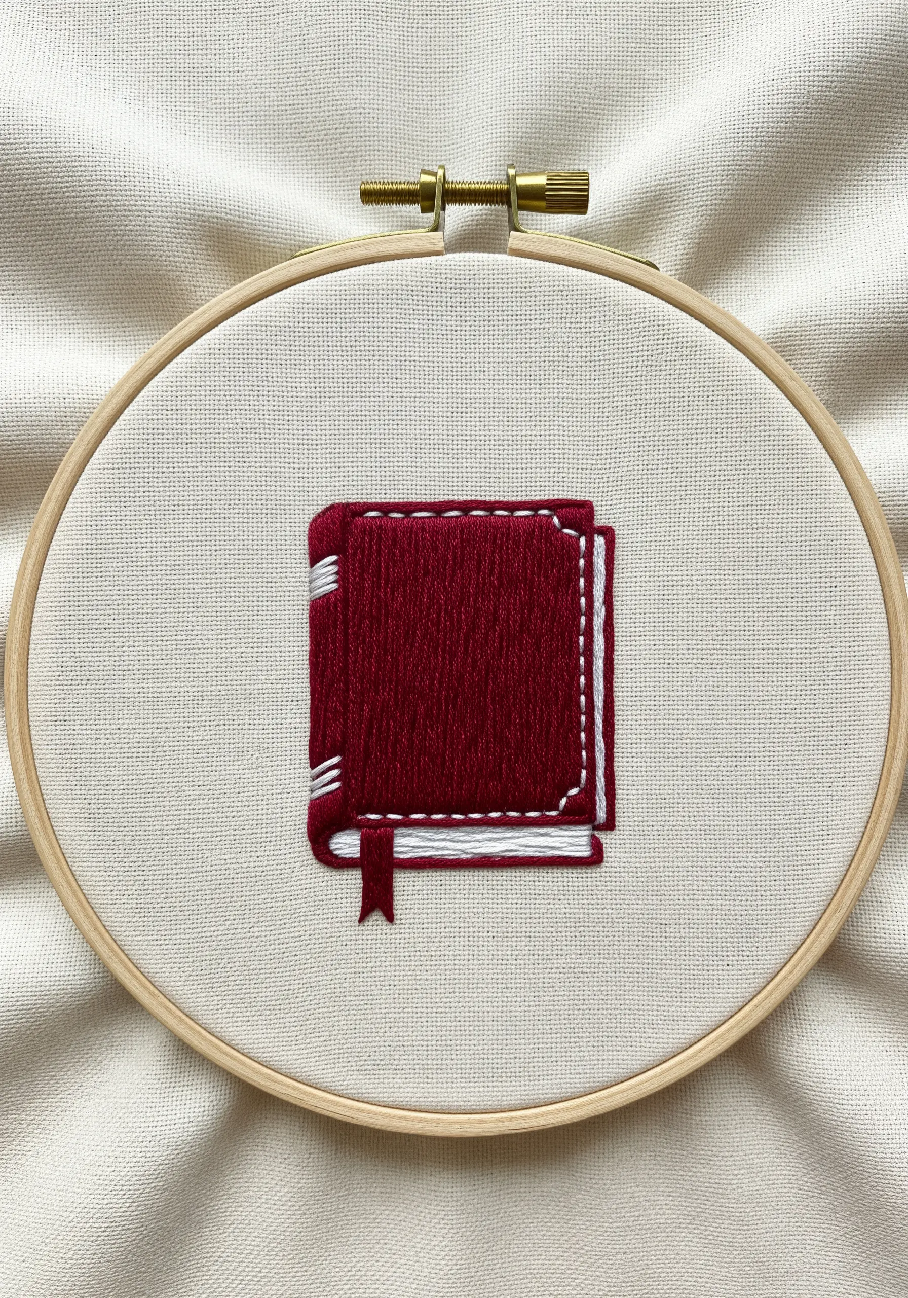 A small red book embroidered with layered satin stitch and white detail stitches.