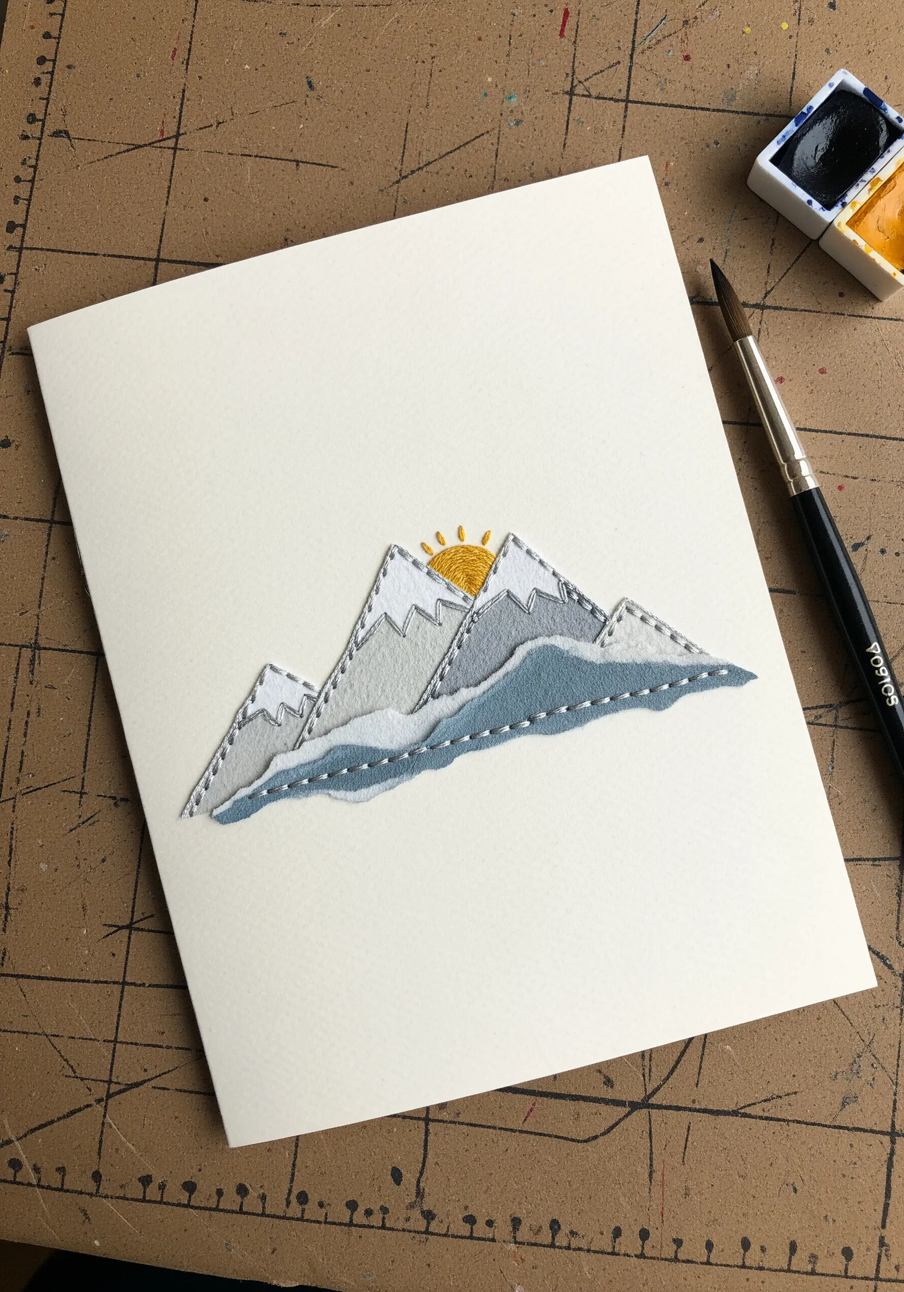Stitched mountain landscape made from layered paper and fabric on a greeting card